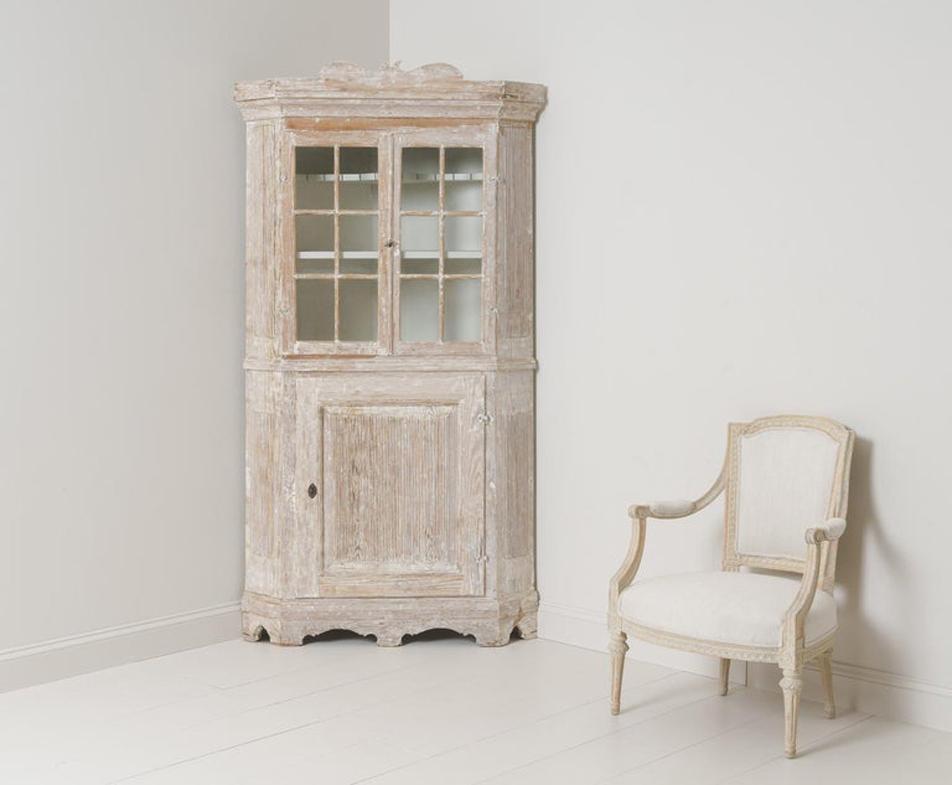 A late Baroque period corner vitrine cabinet from the 18th century in hand - scraped original paint with a scalloped base and reeded sides and lower door. Original lock with key and original glass. The upper section contains two shelves, the top