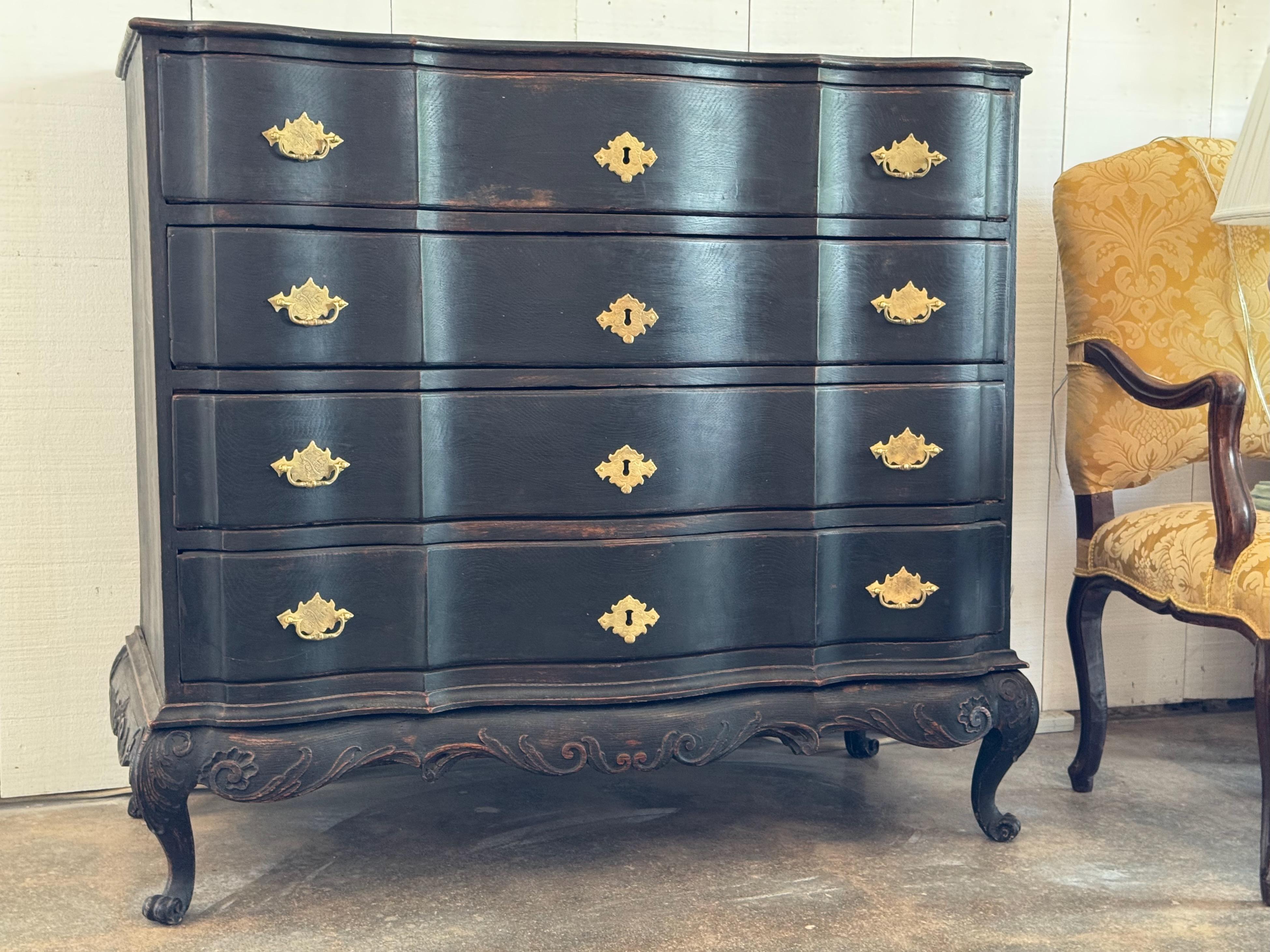 18th century Swedish chest with a bold serpentine front and black painted finish, showing soft wear along the edges. Carved cabriole legs with paw feet and scrollwork apron add Baroque character. Brass escutcheons and drawer pulls contrast elegantly