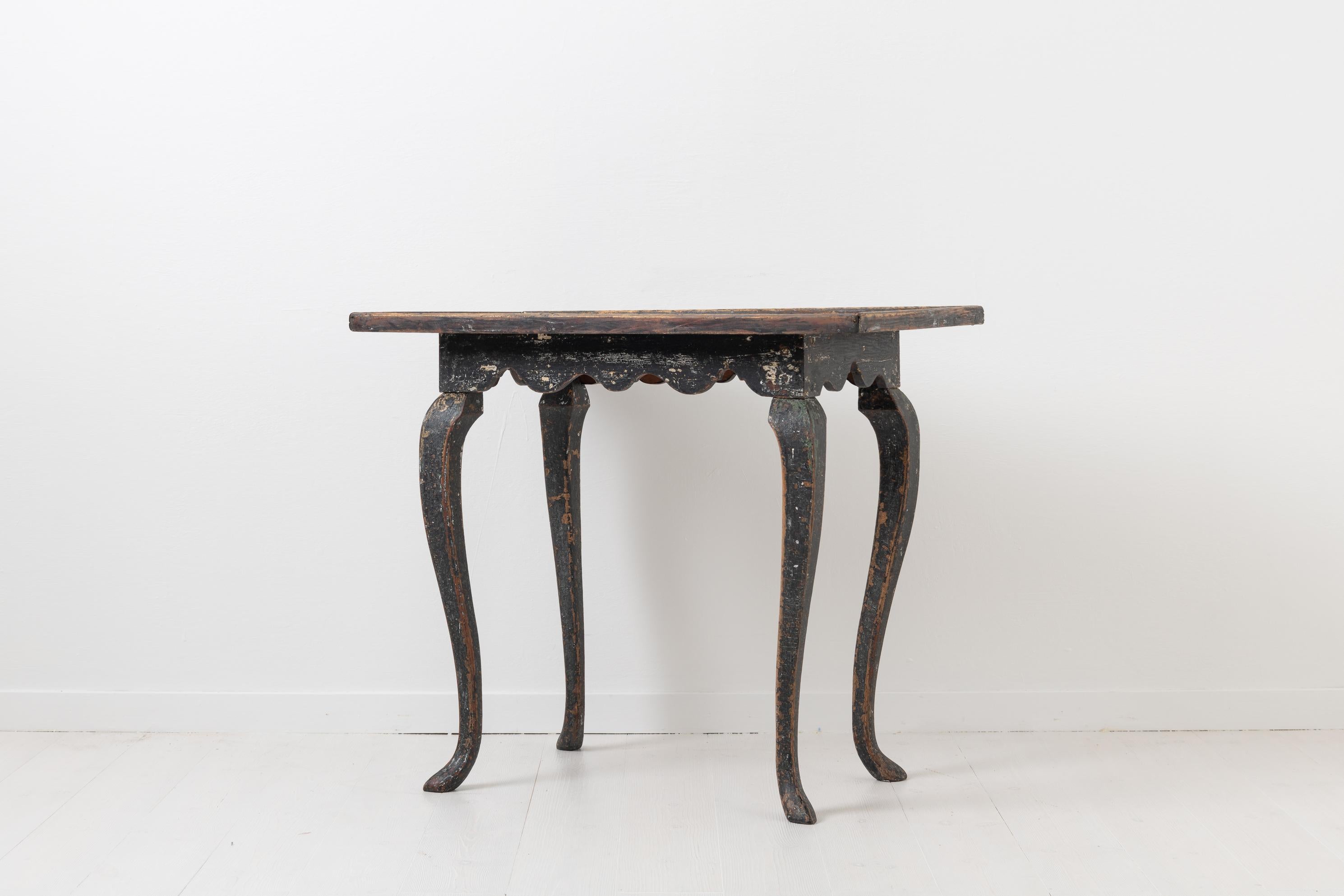 Swedish rococo table with black historic paint. The table is made in northern Sweden circa 1770 from Swedish pine. It was painted black during the 1800s and the paint has since then become distressed with traces of an older light paint showing
