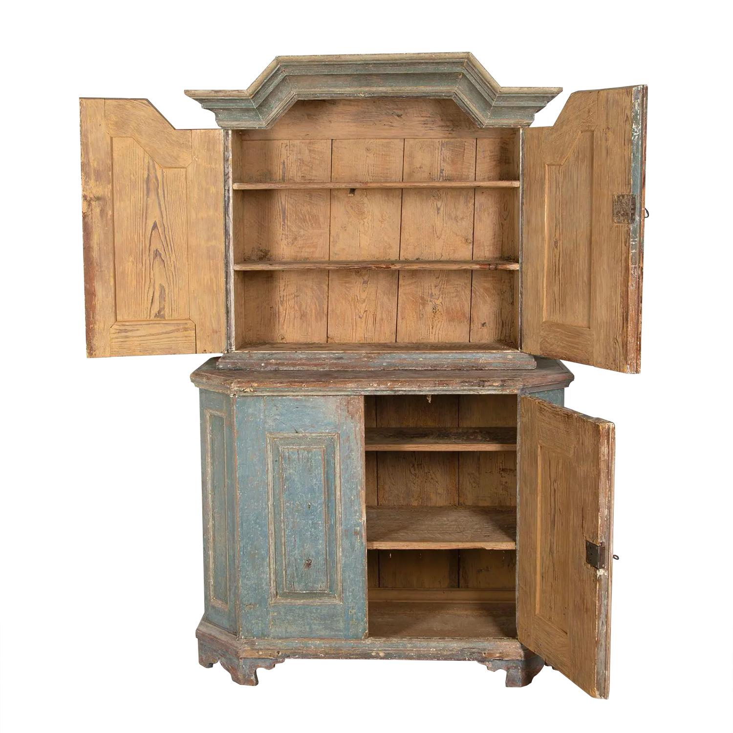 Swedish two part cabinet with a decorative deep pediment. The top portion opens to shelving for storage. The bottom section features decorative panelling to the four panels, opening to further storage. This piece has been dry scraped to original