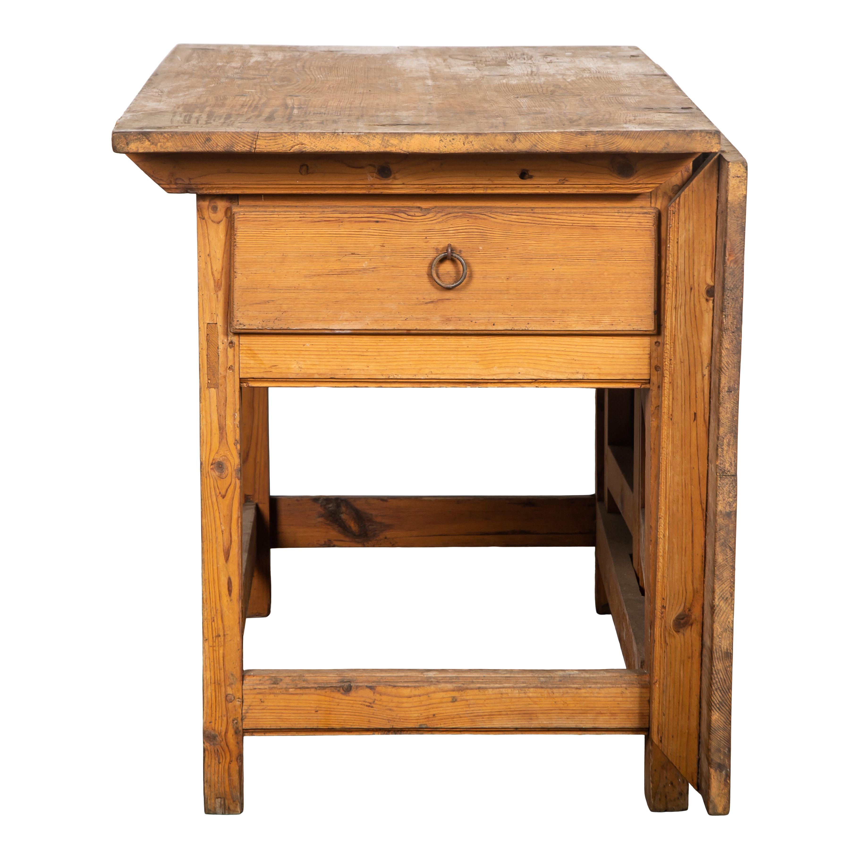 An 18th century vintage wood drop leaf table with one large drawer from Sweden. This classic wood table features one large drawer with a metal ring pull that can be used for addition storage. The simple wood design features straight legs and a thin