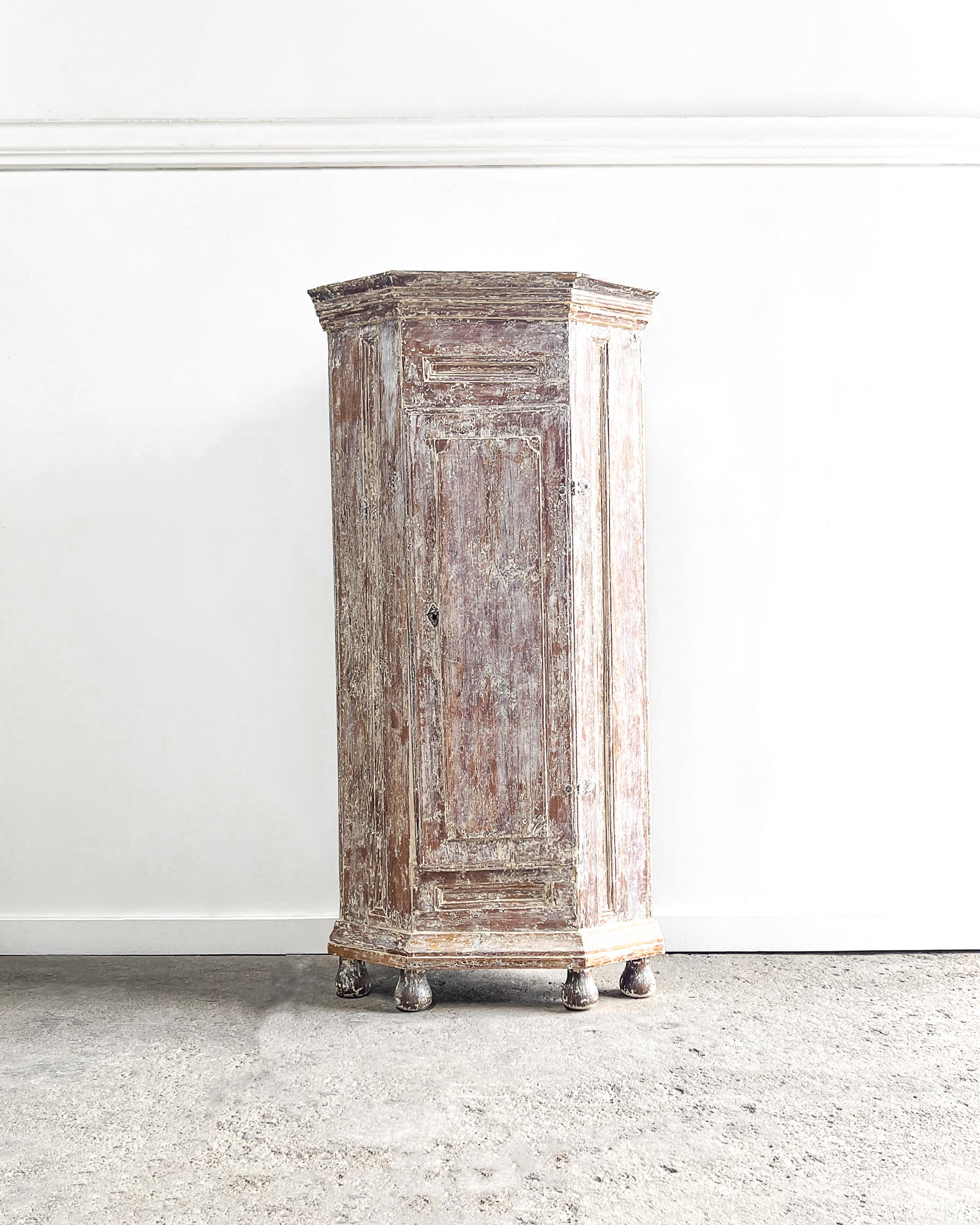 A lovely Swedish encoignure (corner) cabinet has a single door that opens to reveal three shelves. 

The cabinet features a beautiful dry-scraped finish having layers of the original creamy white and blue-gray paint revealing areas of the natural