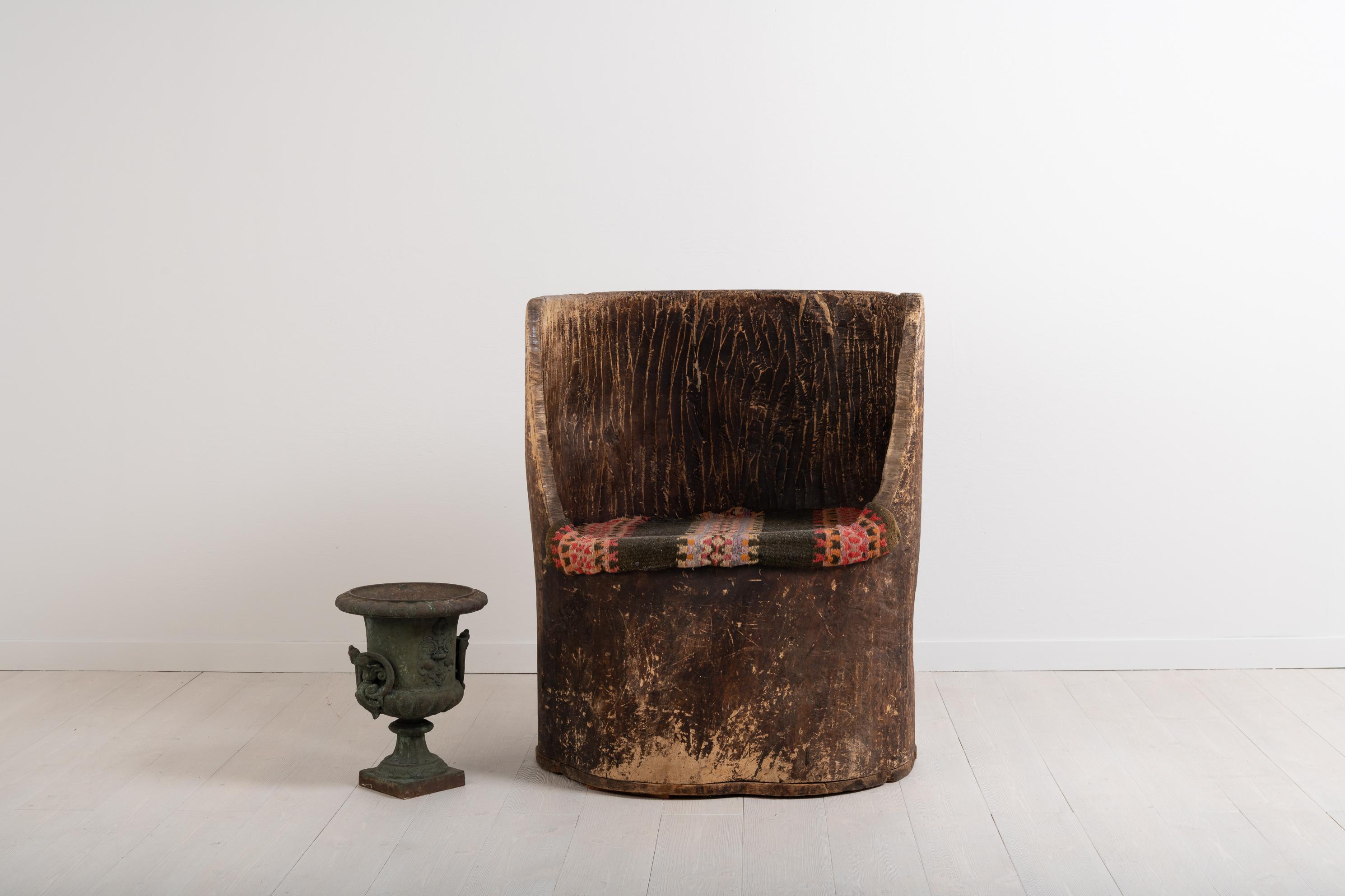 Swedish Folk Art kubbstol manufactured from a single piece of wood. The log has been hollowed out and shaped into a chair. Because of the material the shape is organic and slightly irregular. Old-fashioned with visible marks from the tools used to