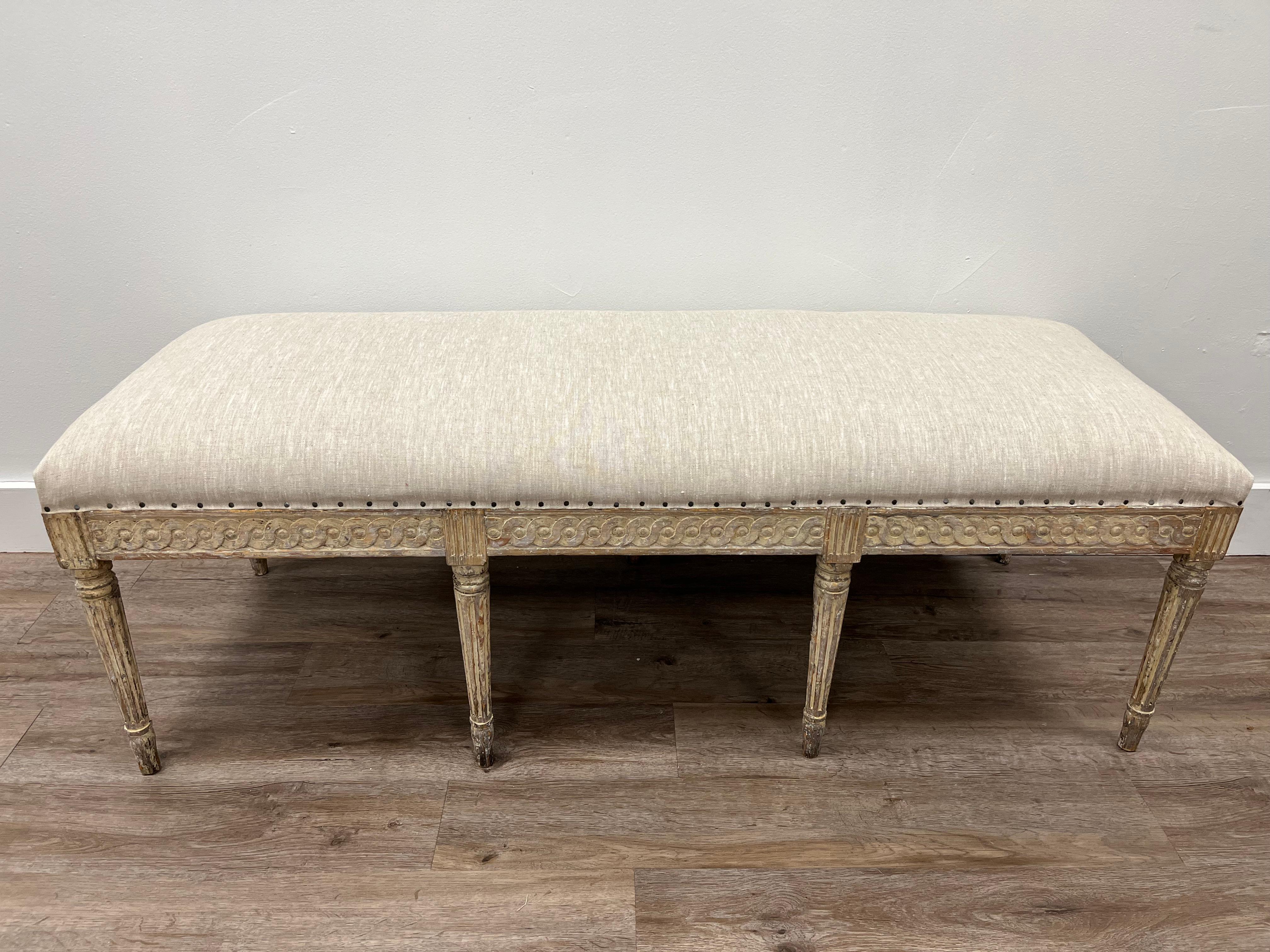 A beautiful Swedish Gustavian bench. Featuring a decorative hand-carved Guilloché scrolling apron on the front and sides with reeded fleurons in between. Legs are tapered and fluted. Meticulously scraped to its original pale yellow paint and
