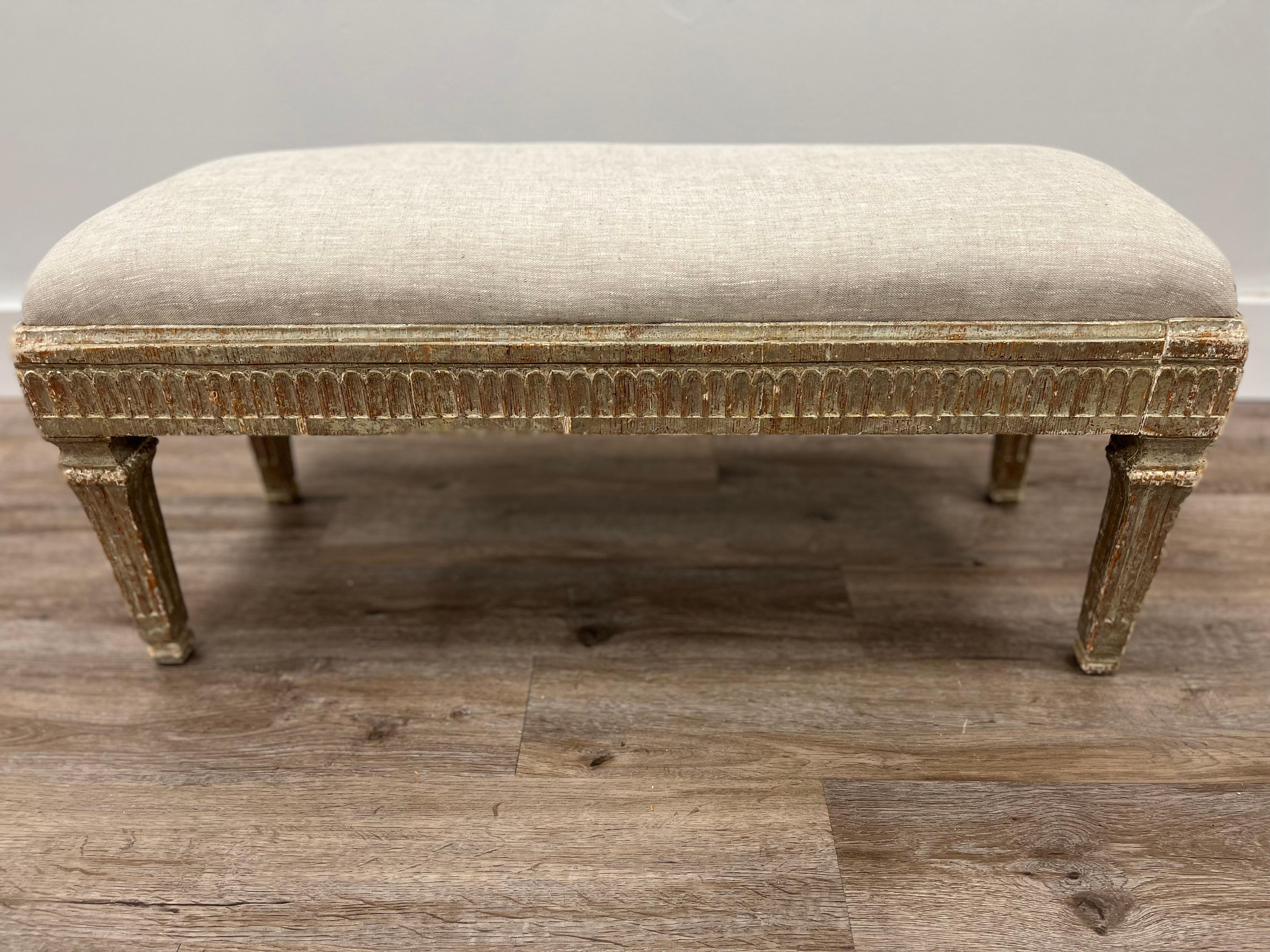 A rare and exceptional low Swedish Gustavian bench featuring leaf cut design on all four sides. Sits atop square, tapered and fluted legs. Meticulously scraped to its original grey paint. The original slip seat has been reupholstered in linen.