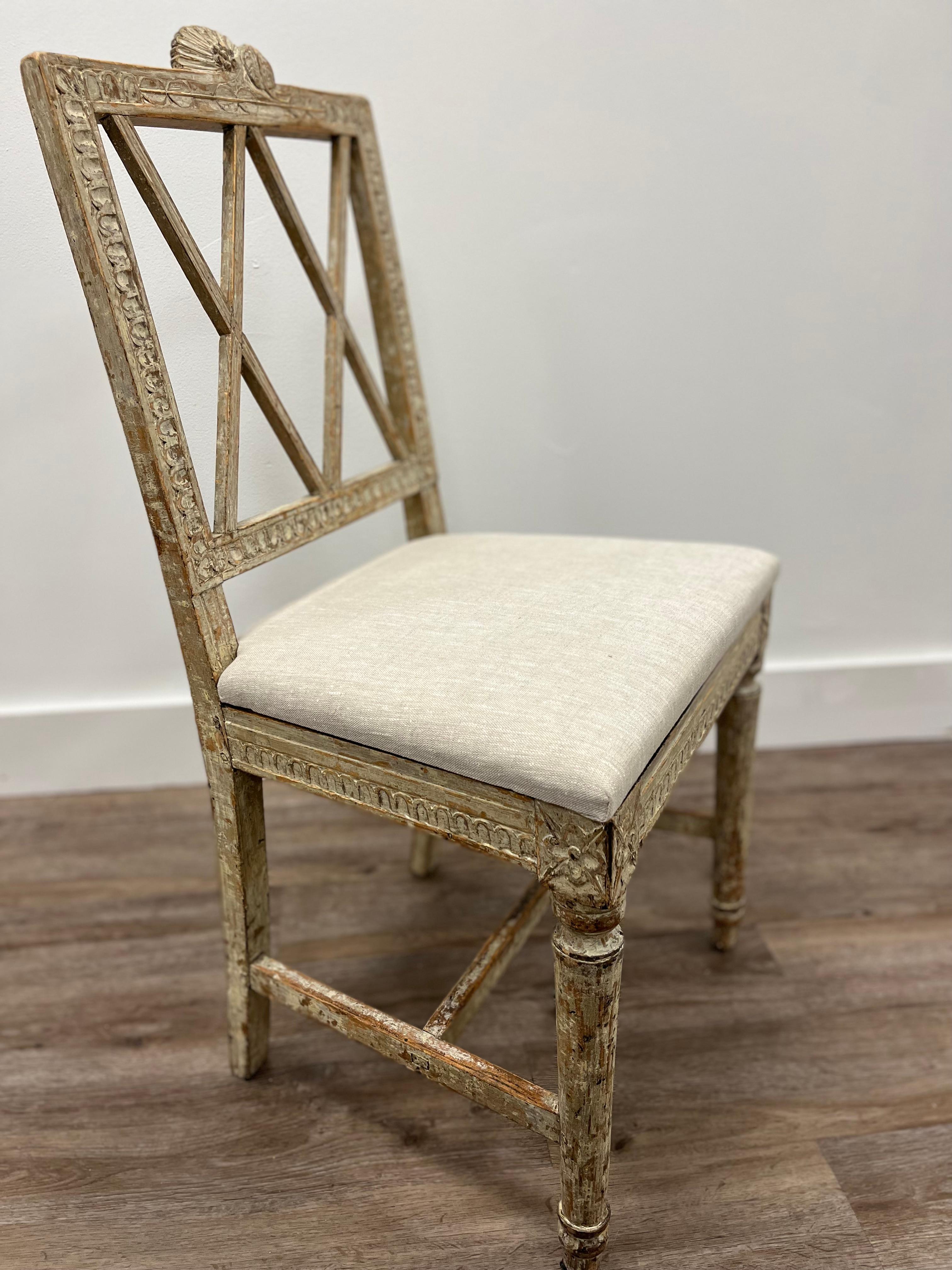 An 18th century Swedish Gustavian chair made in Lindome. Featuring a square backrest framed with leaf cut design on three sides and topped with a floral hop and leaf cut crown. Crisscross design frames the interior. The base has additional leave cut