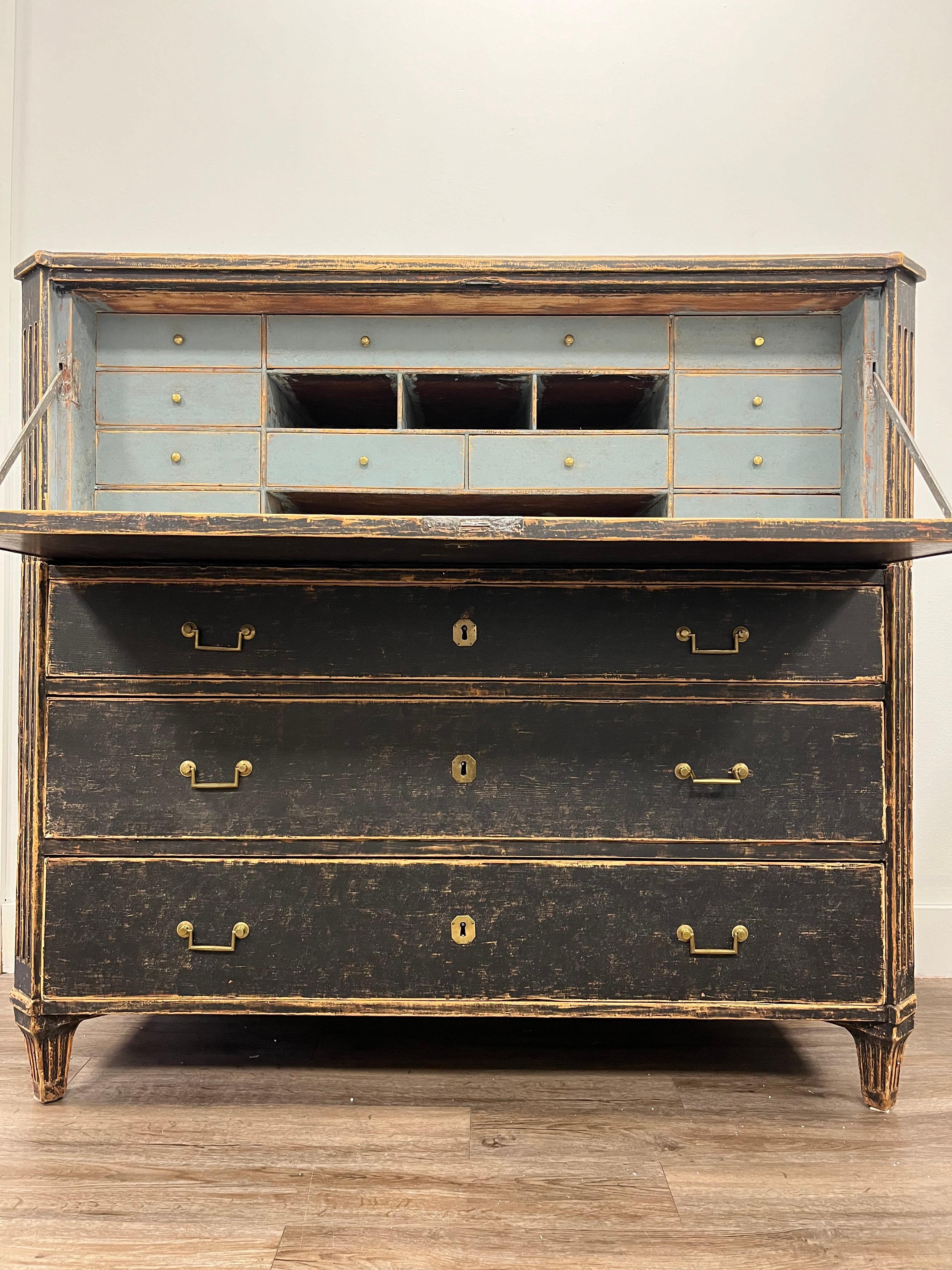 A two part Swedish Gustavian fall front desk. Upper section top opens to an ample work surface, eleven drawers with brass pulls and four storage cubbies. The lower section has three large drawers. Front corners are canted and fluted. Back corners