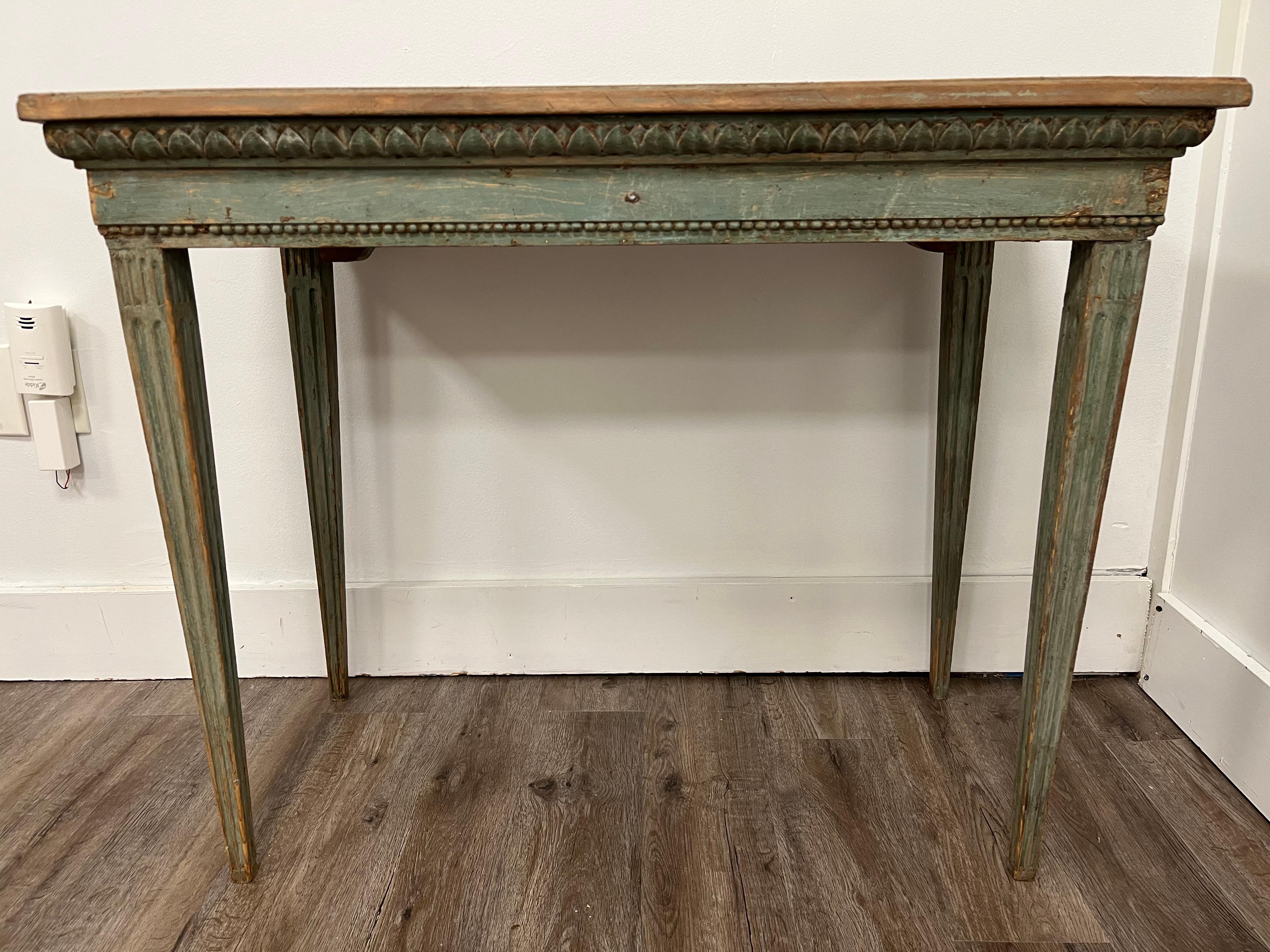 A Swedish Gustavian game table meticulously scraped to its original pale green color. Top removes to reveal original game board. Frame is decorated with intricate vertical leaf cut carvings and adorned with beaded details across the front and sides.