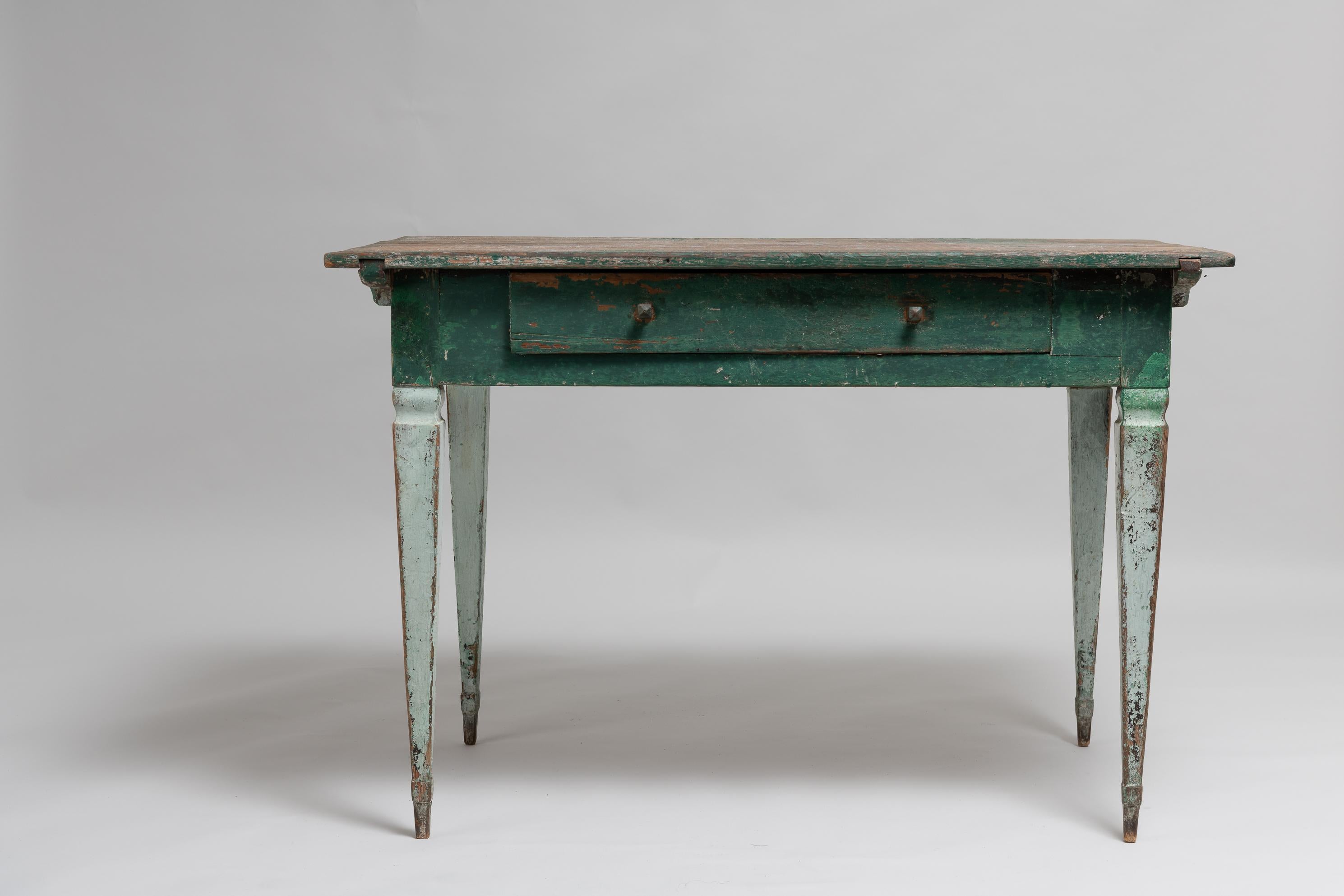 18th century green gustavian desk in painted pine. Old historic paint from the 1800s with visible distress and patina. Hand made wooden handles to the drawer. An unusual detail is the collar around the legs down by the feet. The table is from the