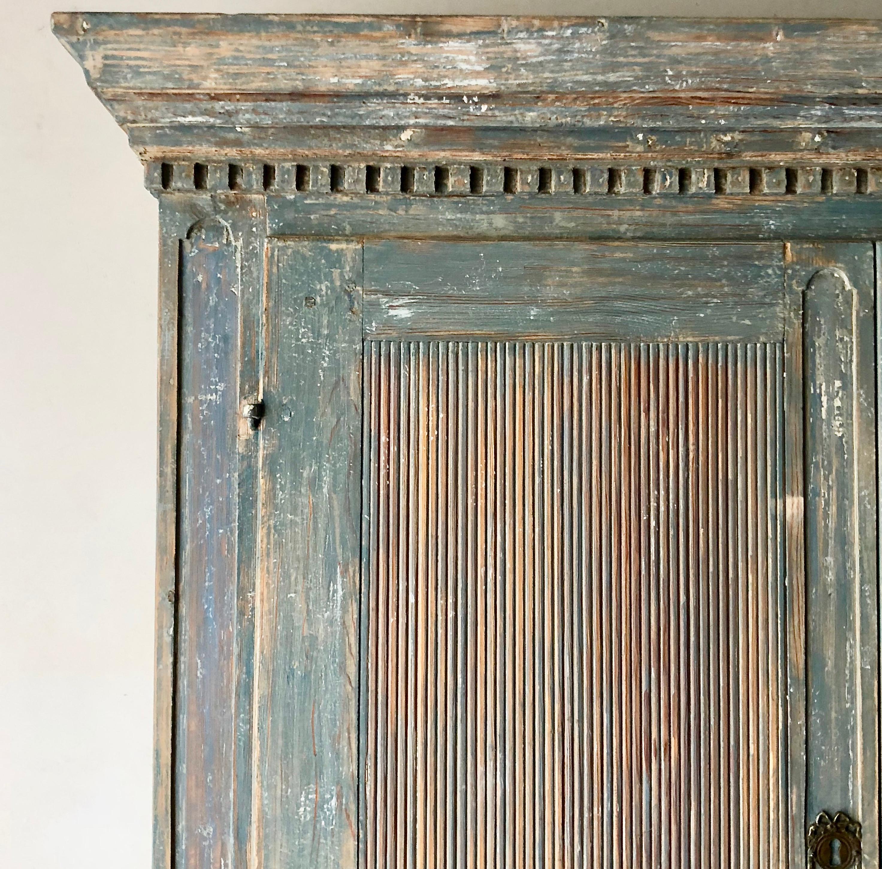 18th century Swedish Gustavian painted cupboard with richly carved, reeded door panels and the simple cornice with dental carvings. Lot of storage with inside selves and small drawers. All in lovely pale blue patina. 
Measurements are with