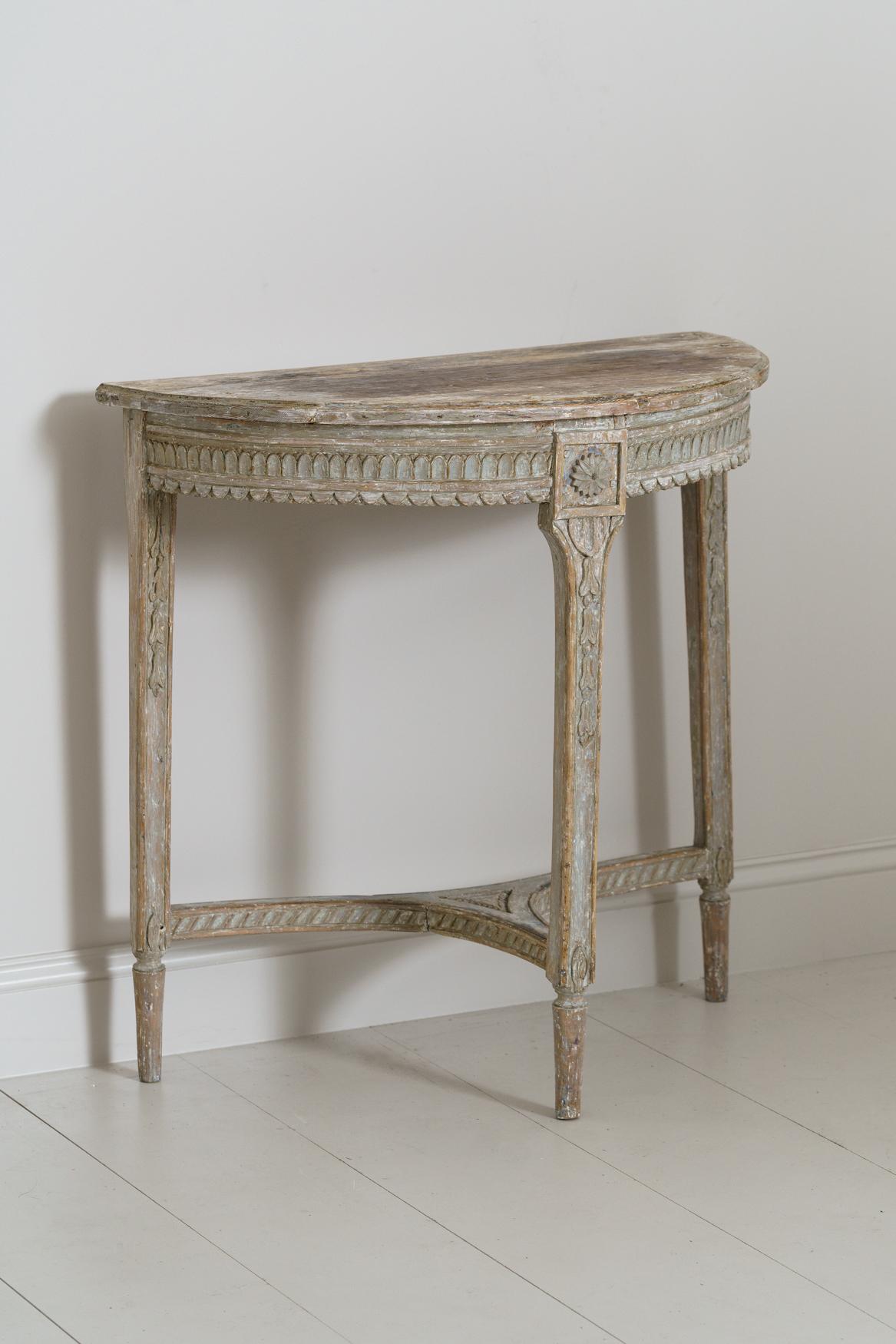 A Swedish Gustavian period demilune table in original blue paint from the 18th century. The apron has egg and dart detail along the top with scalloped detail below. Cascading bell flowers on each leg below carved rosettes.