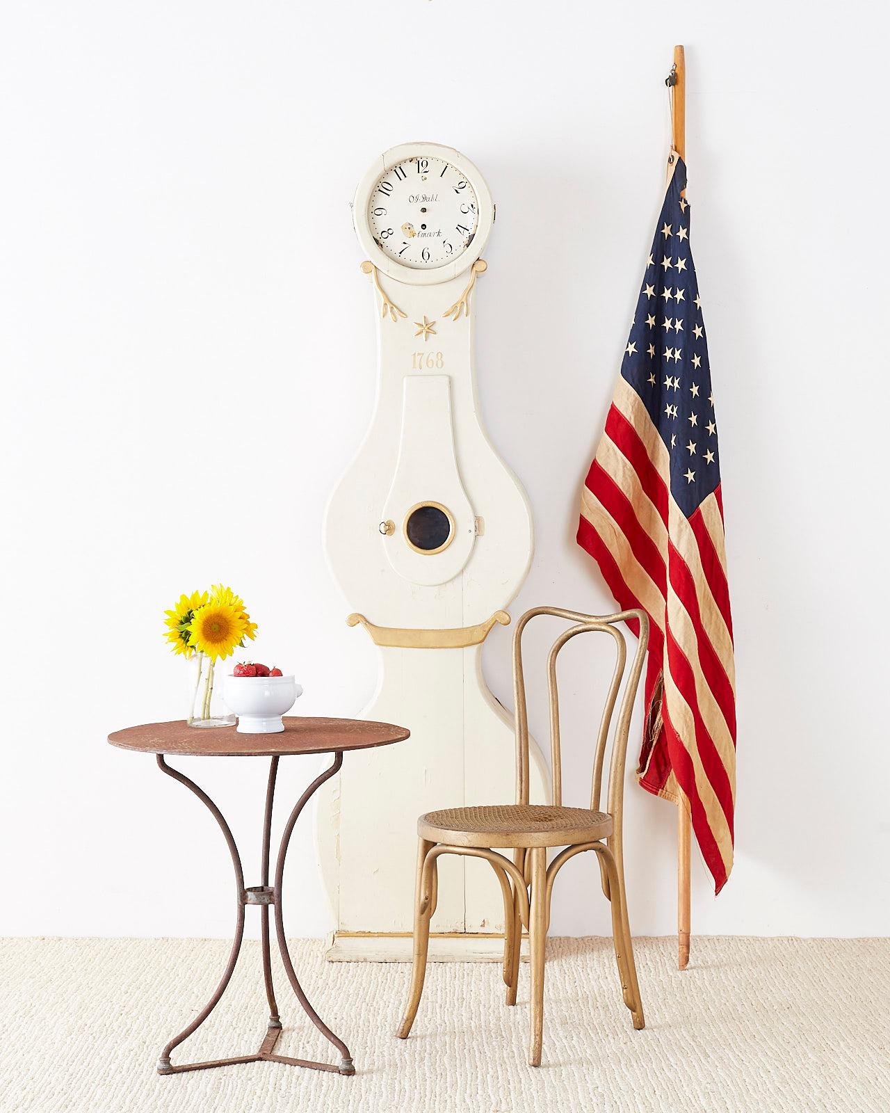 Attractive 18th century Swedish long case mora clock from the Gustavian period. Features a white lacquered case with decorative parcel-gilt accents. The middle of the case has a windowed door to access the inside. Round top holds an enameled face