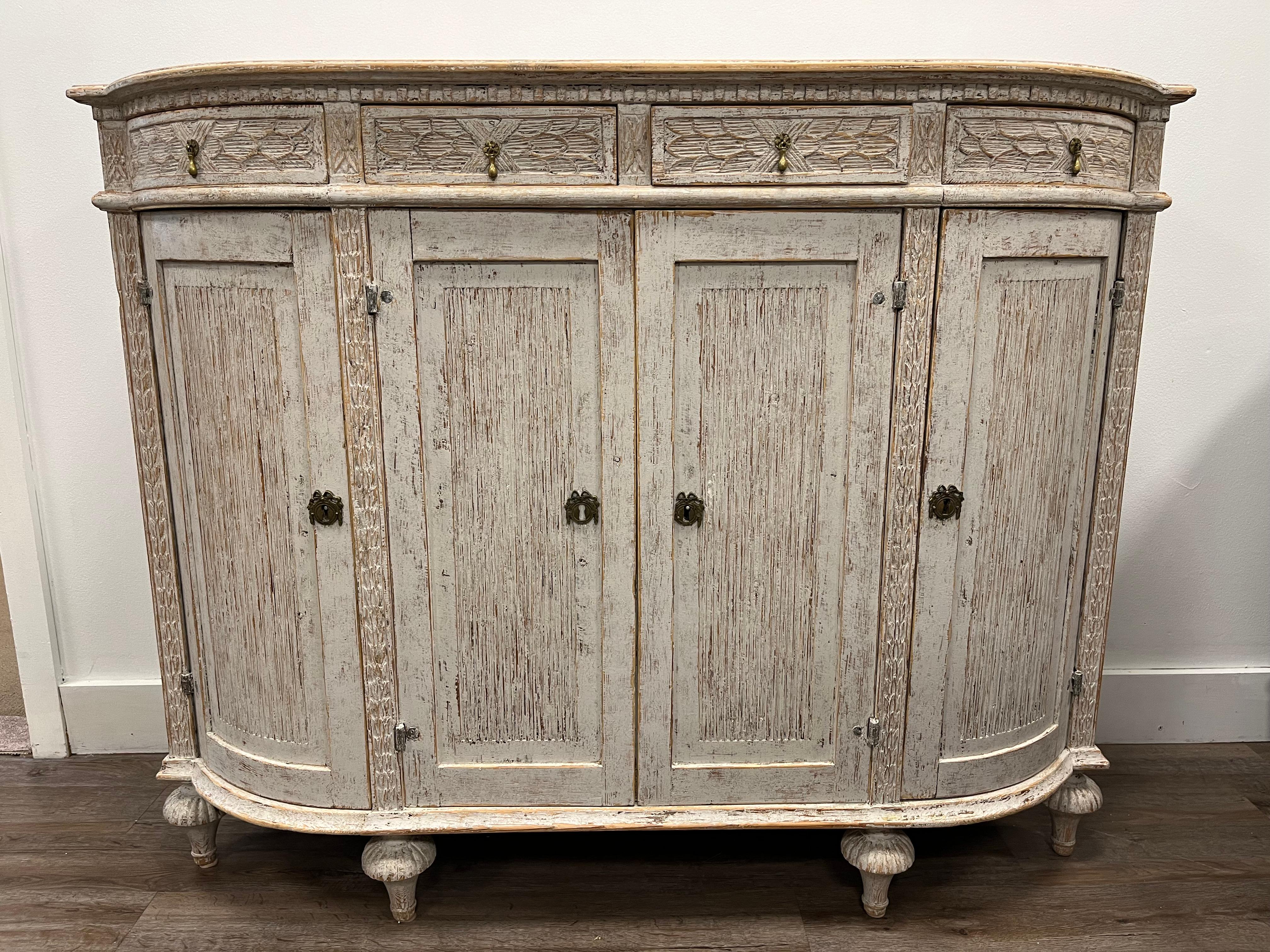 A unique Swedish Gustavian four door sideboard with original brass hardware and locks. Featuring curved corner design, beveled top, decorative hand carved dental detail, elaborate drawer front carvings and vertical reeded front and corner doors. The