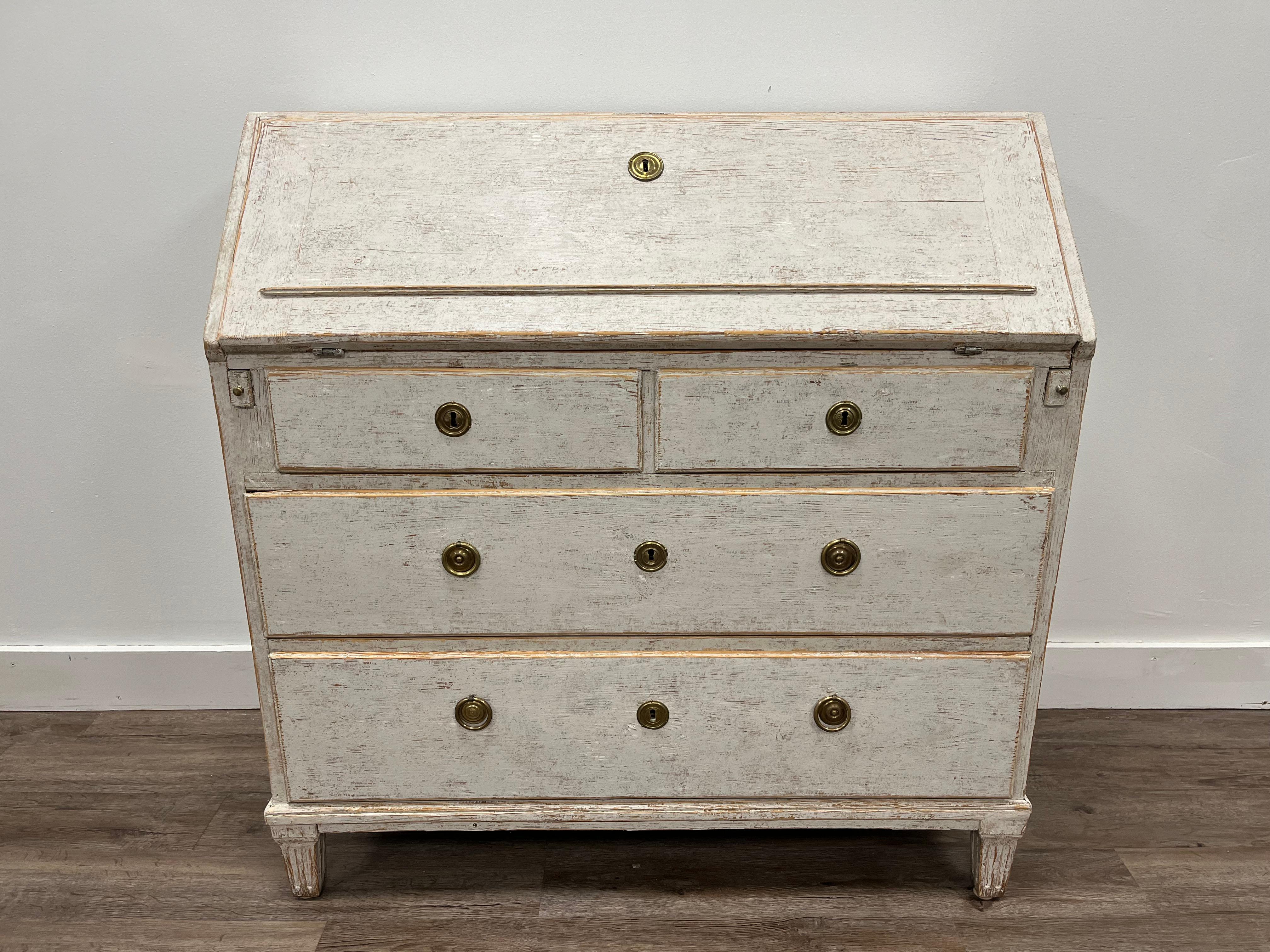 A Gustavian slant front desk. The upper section has eight small drawers, four cubbies, two sliding columns and a small locking door. The lower section has two small drawers over two large drawers. Sits atop fluted rectangular feet. Original brass