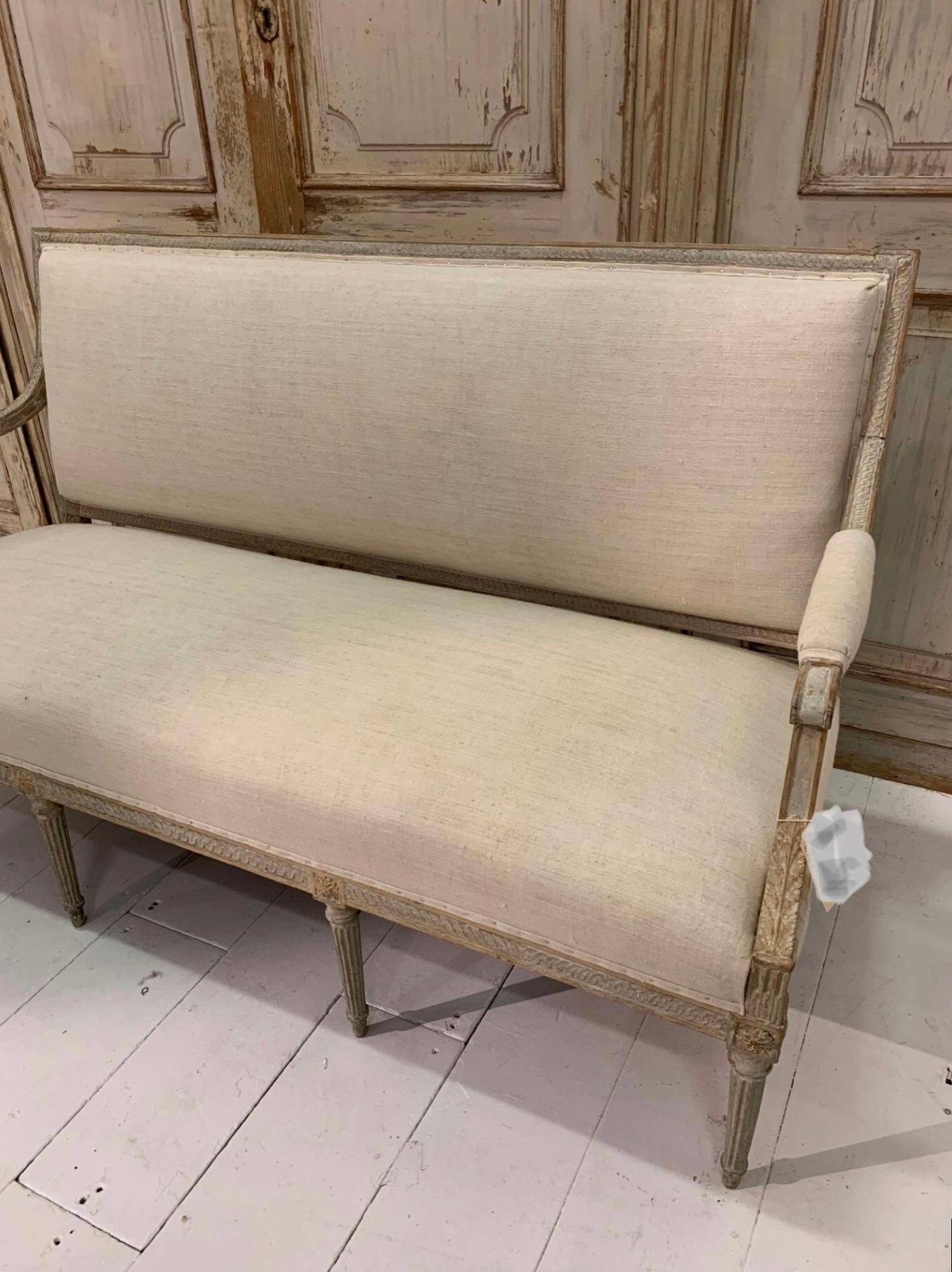 A handsome late c18th Swedish Gustavian painted sofa. that has been hand scraped down to the original paint showing off its classic and understated carved wood detailing. 
Later reupholstered in an off white neutral vintage french linen the seat is