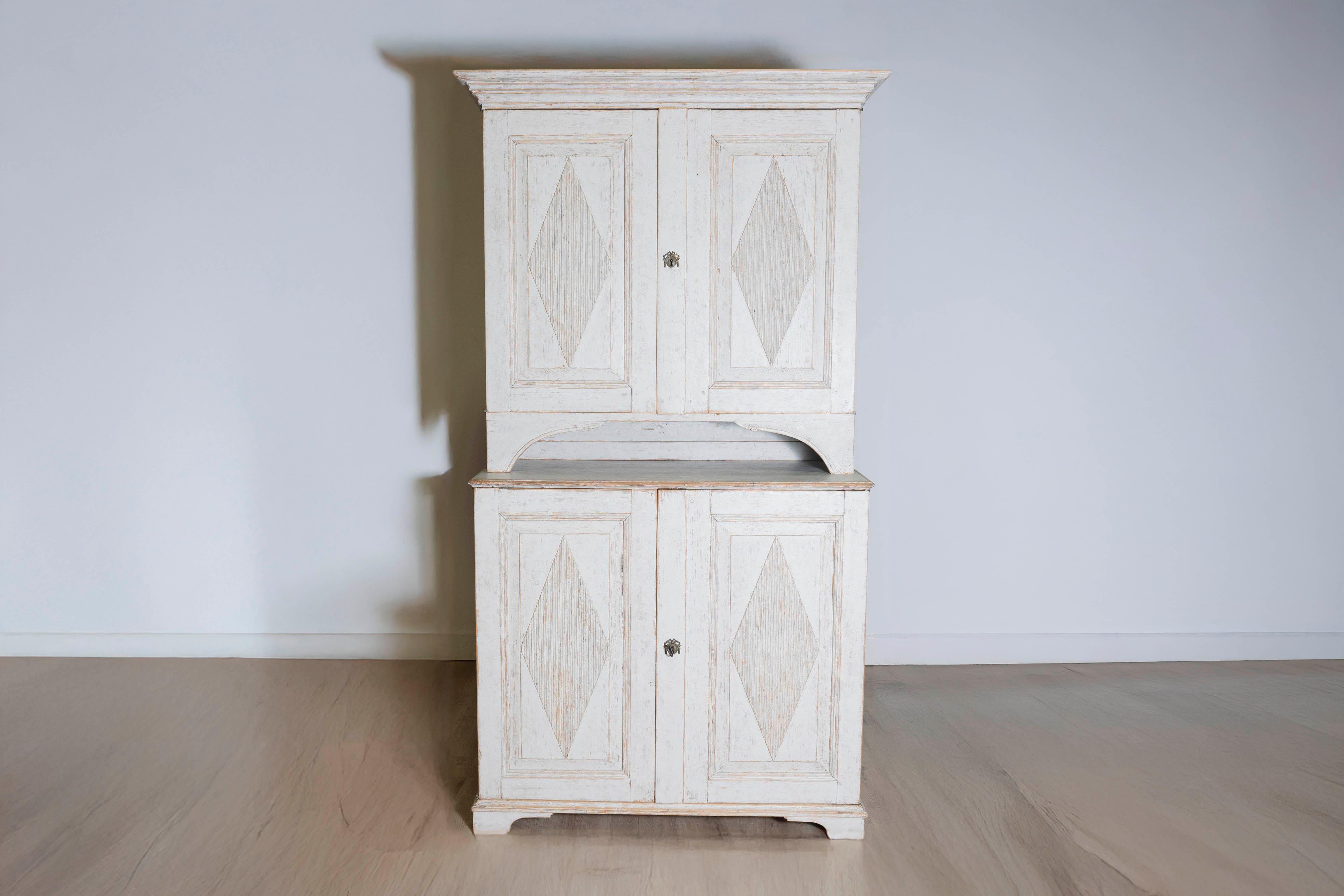 This 18th-century Swedish Gustavian two-part cabinet, circa 1790, is a stunning example of the elegant simplicity that defines the Gustavian style. Crafted from pine, the cabinet features a painted finish in soft, neutral tones, enhancing its light