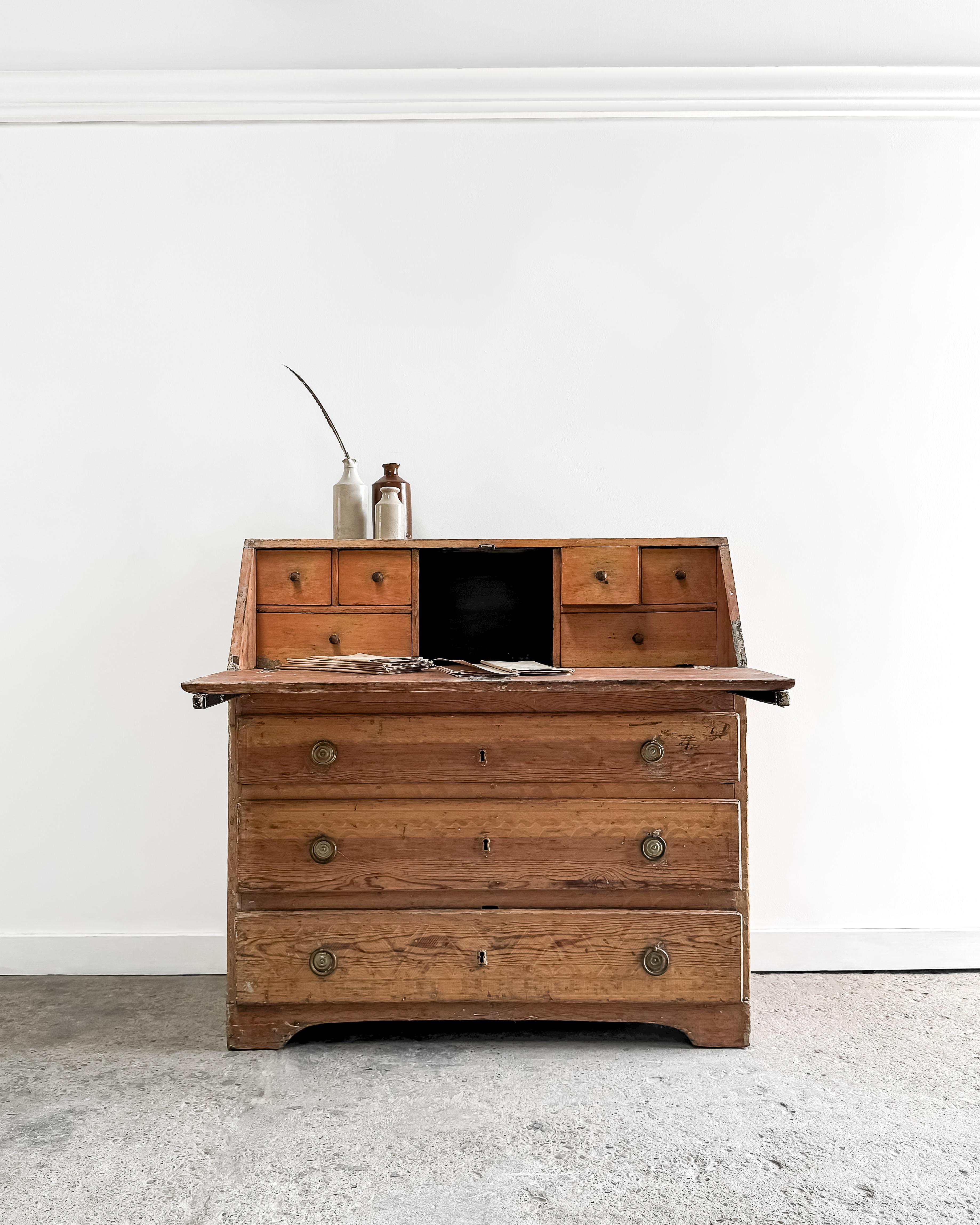 This antique 18th-century Swedish Gustavian writing bureau is a rare and handsome piece, crafted from solid pine. It stands on modest bracket feet, showcasing the original brass ring pull hardware and brass escutcheons. The bureau features three