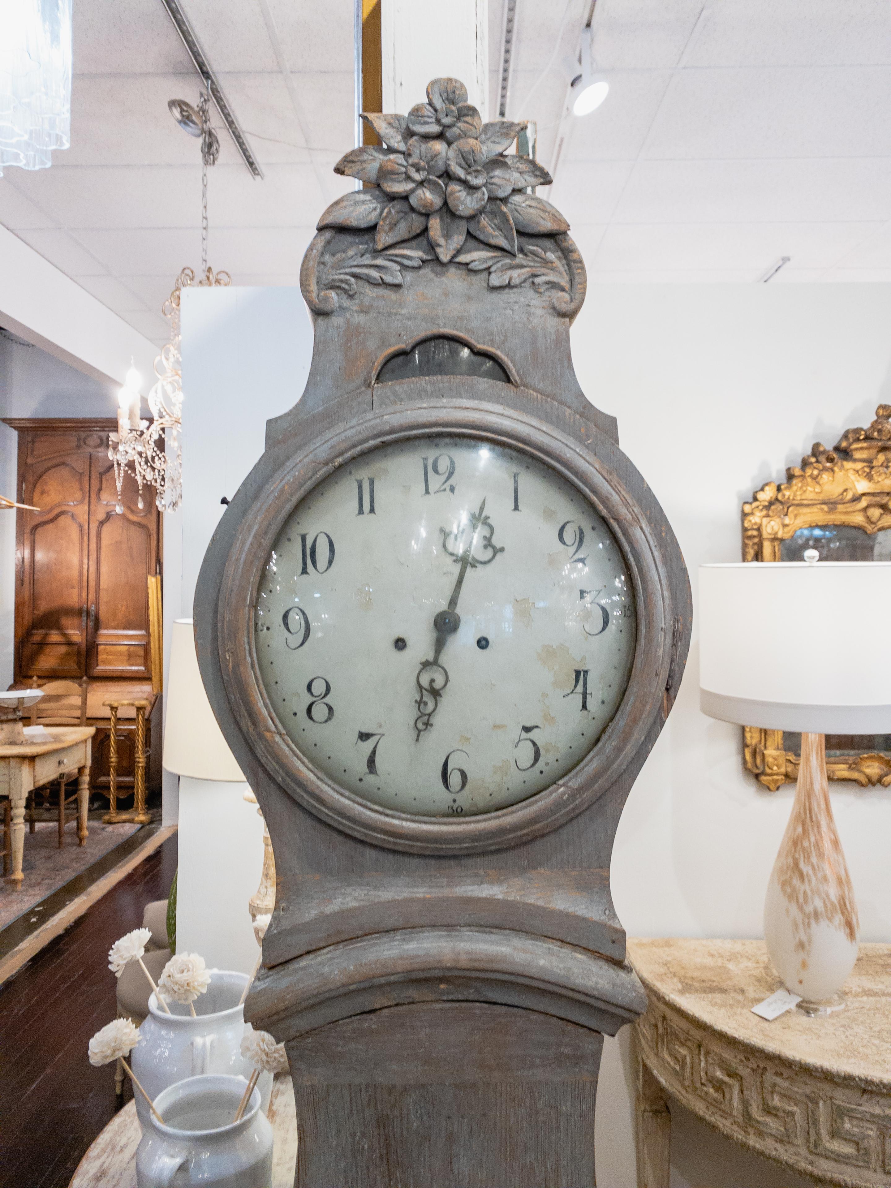 An 18th century Swedish Mora clock is a tall, freestanding clock that originated in the Mora region of Sweden. It typically features an elegant and slender wooden case with decorative carved details. The clock's distressed painted finish suggests