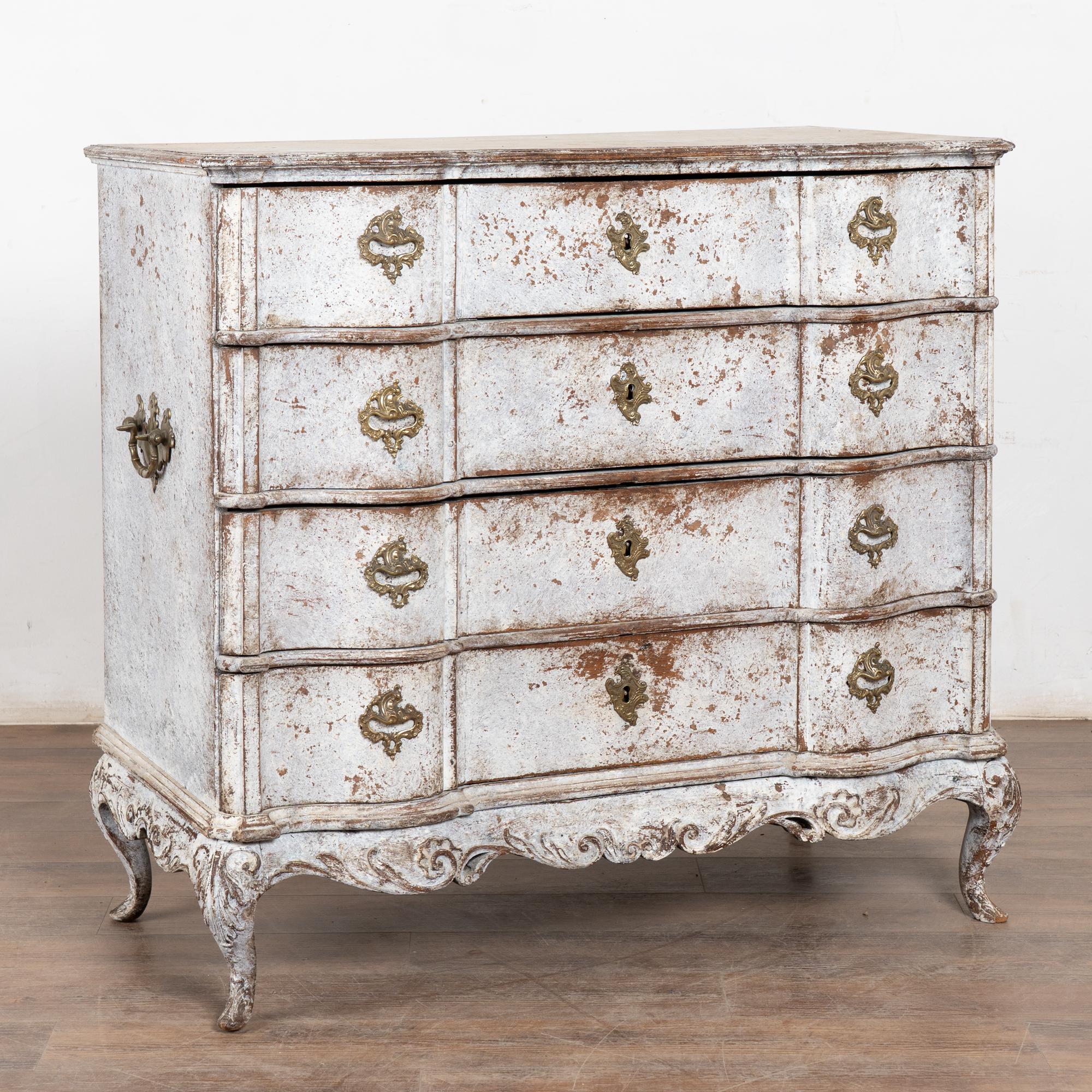 This large antique rococo chest of four drawers features a serpentine front, decorative carved skirt, original brass hardware pulls and rests on cabriolet feet.
It has been given an exceptional new professional antique white layered painted finish