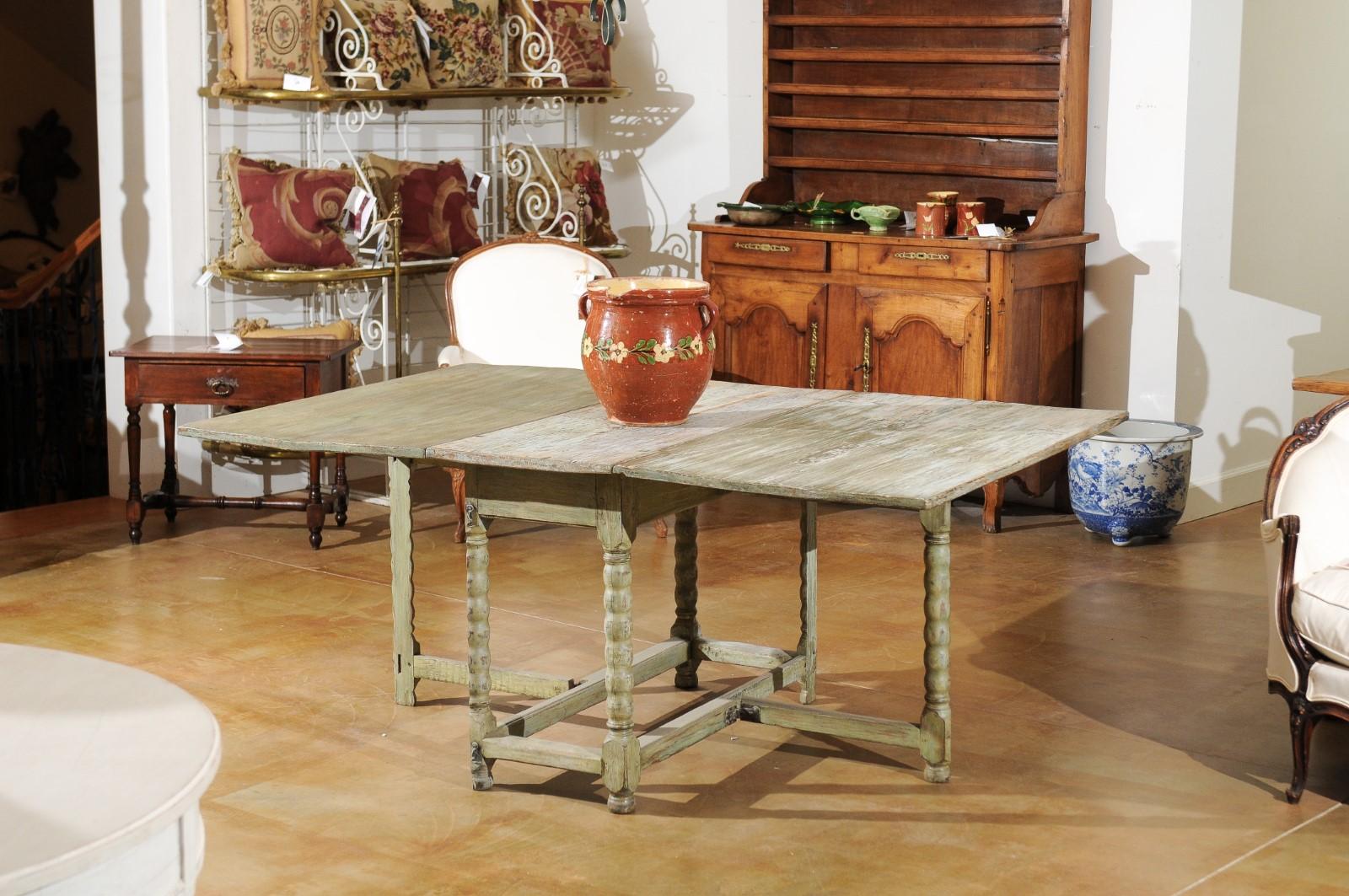 A Swedish painted wood gateleg drop-leaf table from the 18th century, with bobbin legs, side stretchers, lateral drawer and distress finish. Born in Sweden during the 18th century, this charming painted gateleg table features a rectangular top whose