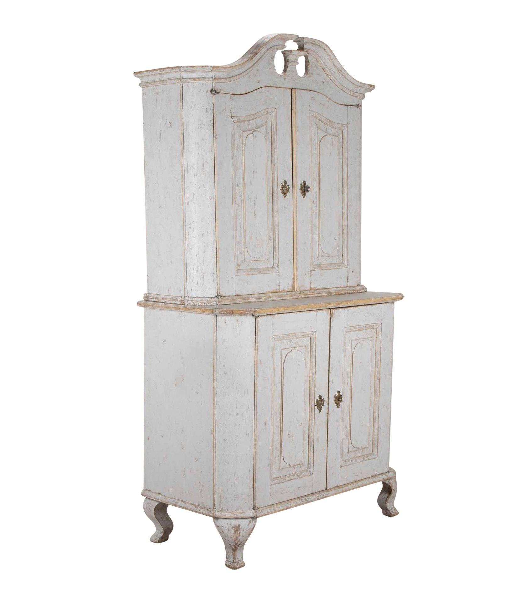 A period 18th Century Swedish two part Rococo cabinet.
With decorative carved pediment and below two carved doors opening to shelved storage. Below, two carved doors with further storage and on cabriolet legs.
Re-painted in soft grey. Circa 1770.