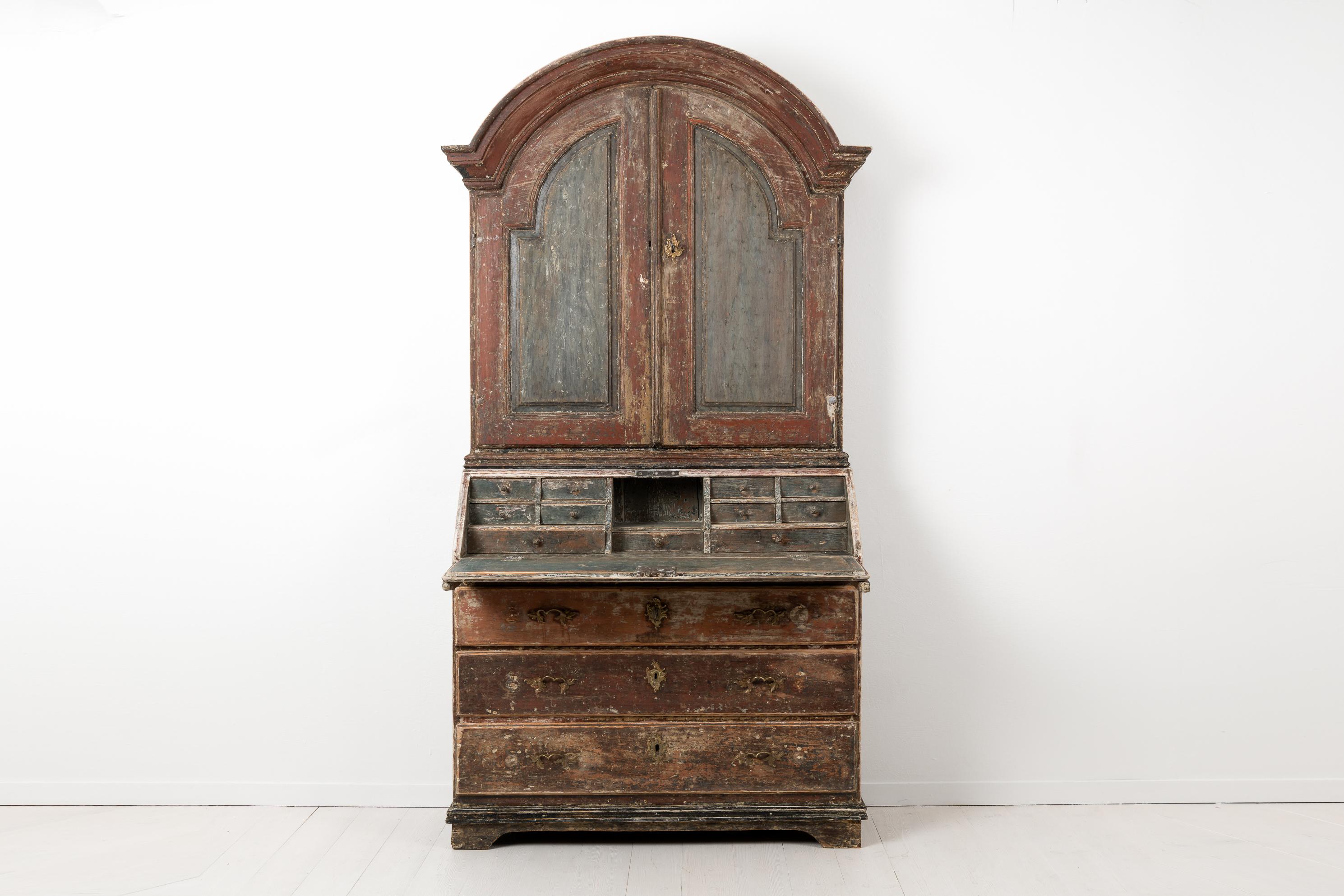 Swedish rococo bureau cabinet from the late 18th century, circa 1780. The cabinet is made in pine and dry scarped by hand with a lot of the original dark paint in tones of red and grey still left. The cabinet is in two parts, the upper cabinet is