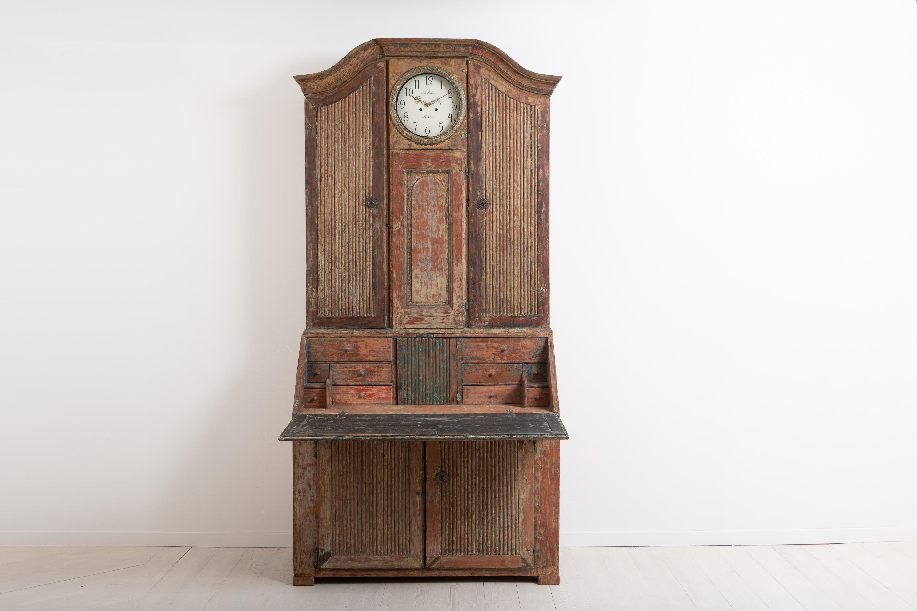 Rococo clock secretary in folk art from northern Sweden. The cabinet - or the secretary - is in two separate pieces and manufactured around the year 1800. It is dry scraped to traces of the original paint and has a rustic patina with natural wear.