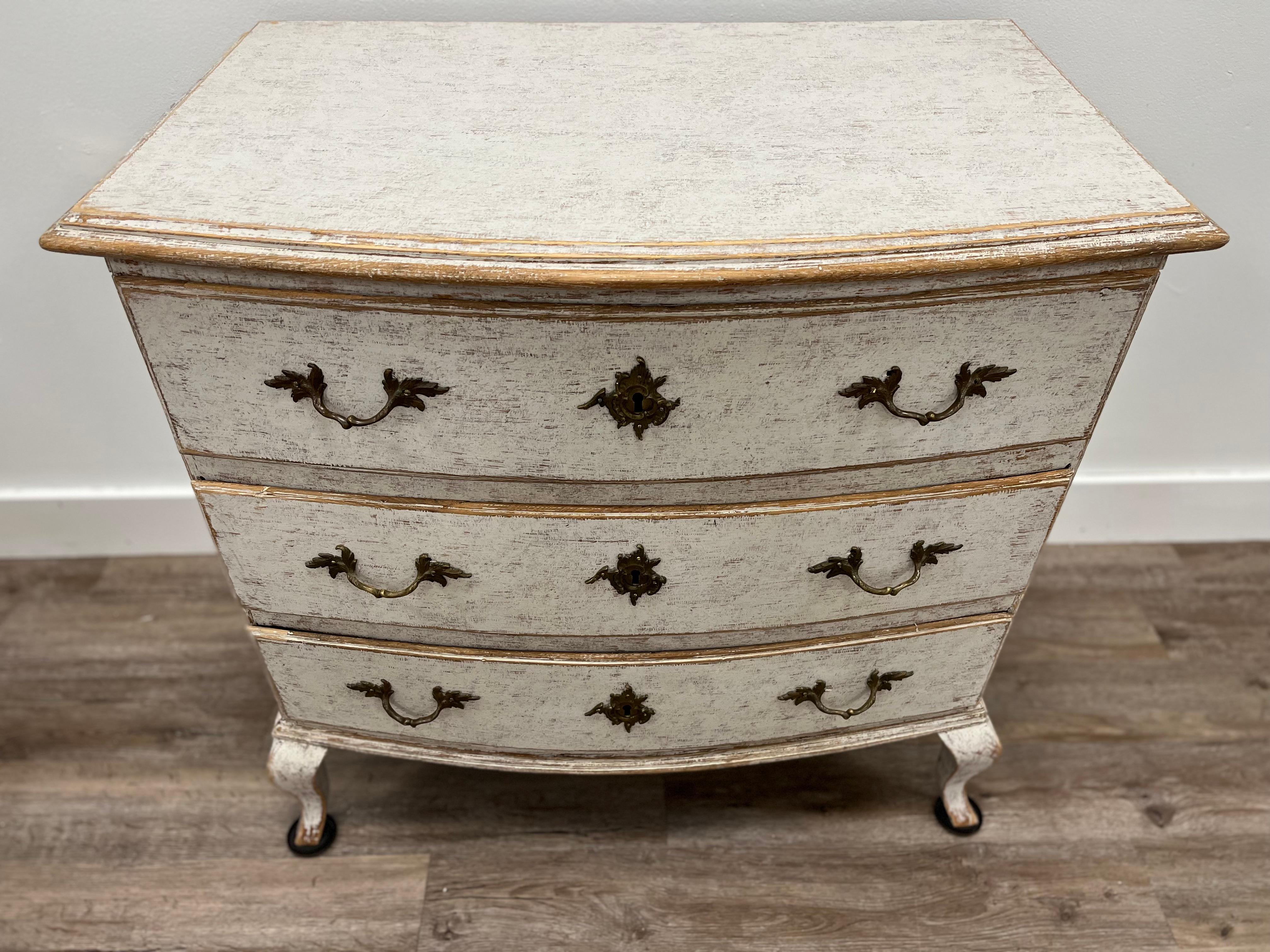 A Swedish Rococo commode repainted in faint pale grey with original brass hardware and locks. Three bow front drawers over cabriolet legs.