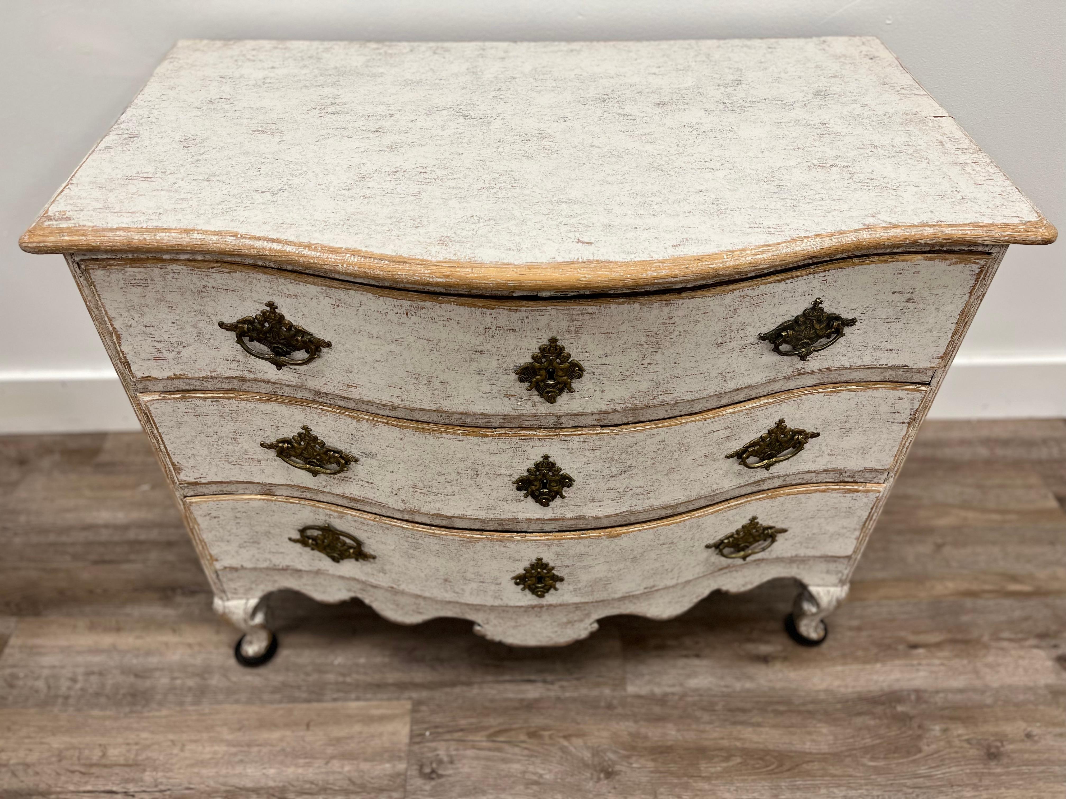 A diminutive bow front Swedish Rococo commode. Three drawers over a carved skirt; sits atop cabriole feet. Original brass hardware and locks. Tastefully repainted in pale greyish-white. 