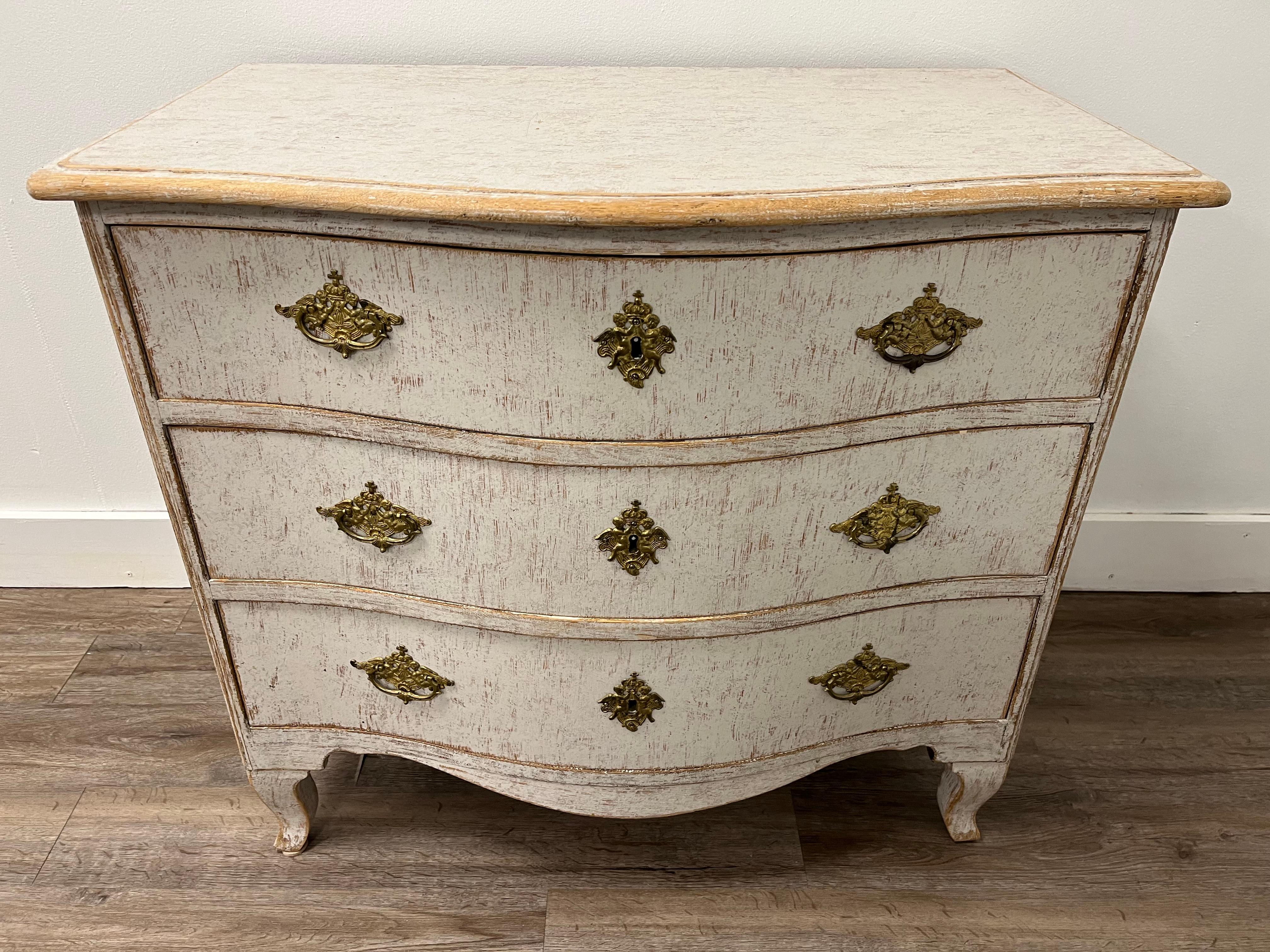 A three drawer Rococo commode with original cherub adorned brass hardware and iron locks. Featuring a bow front and cabriolet legs. Tastefully repainted in soft white-grey. 