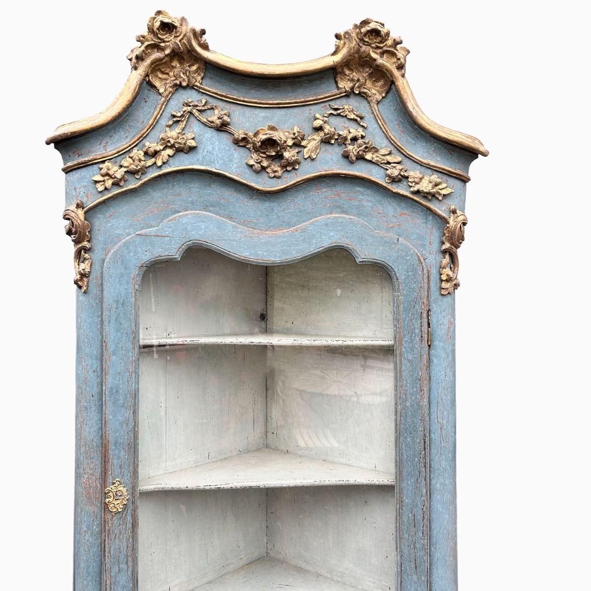Elegant Swedish Rococo corner display cabinet in two parts, showcasing exquisite craftsmanship and refined details.
Crafted from pine wood and painted in a soft rococo blue.
Beautifully adorned with hand-carved decorations featuring rocaille motifs,