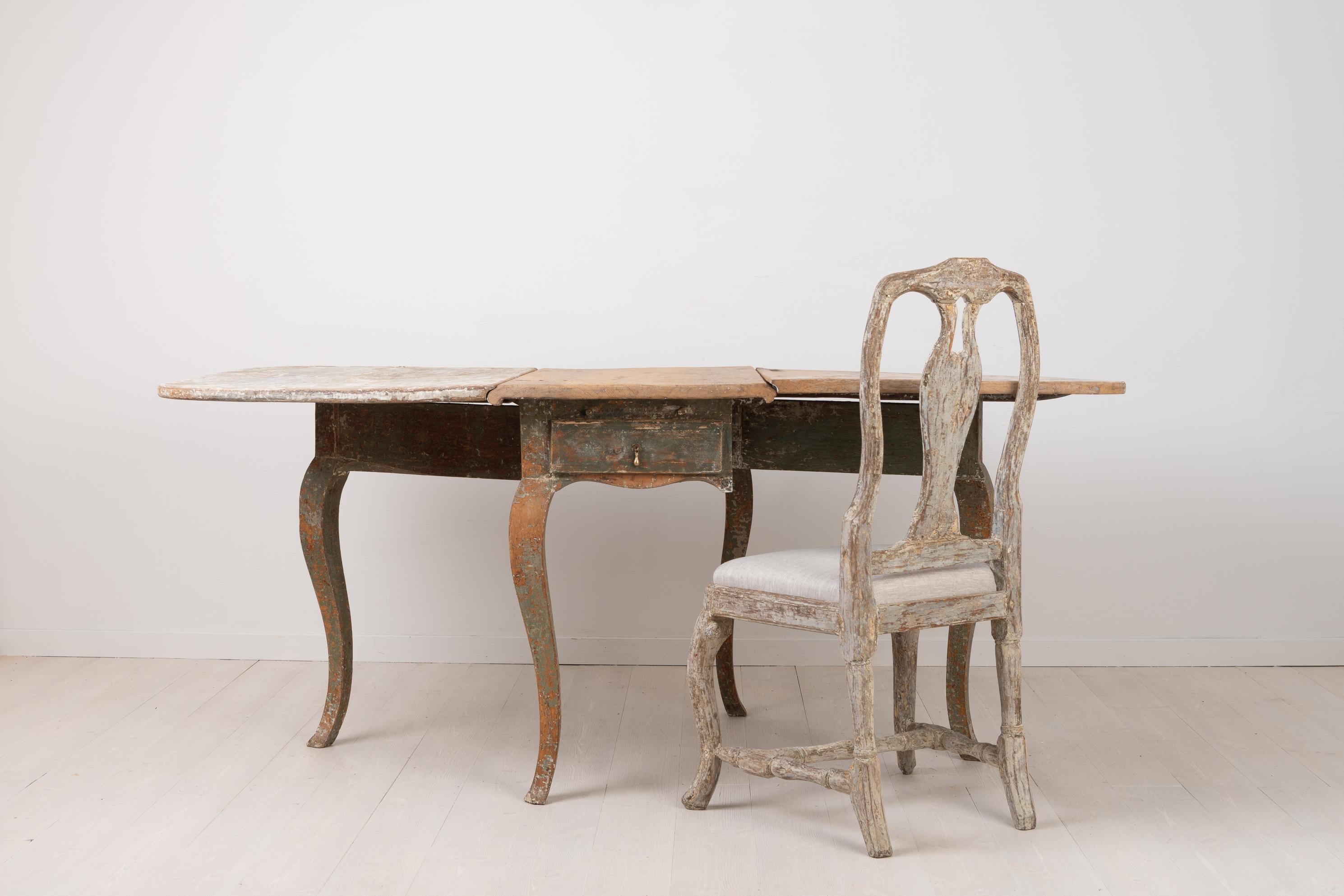 Unusual drop-leaf table in Rococo from Sweden. The table is made circa 1770 and has double leafs and fold out legs. Dry scraped by hand down to the original first layer of paint. The table tops have quite a lot of wear on the paint. Drop-leaf tables