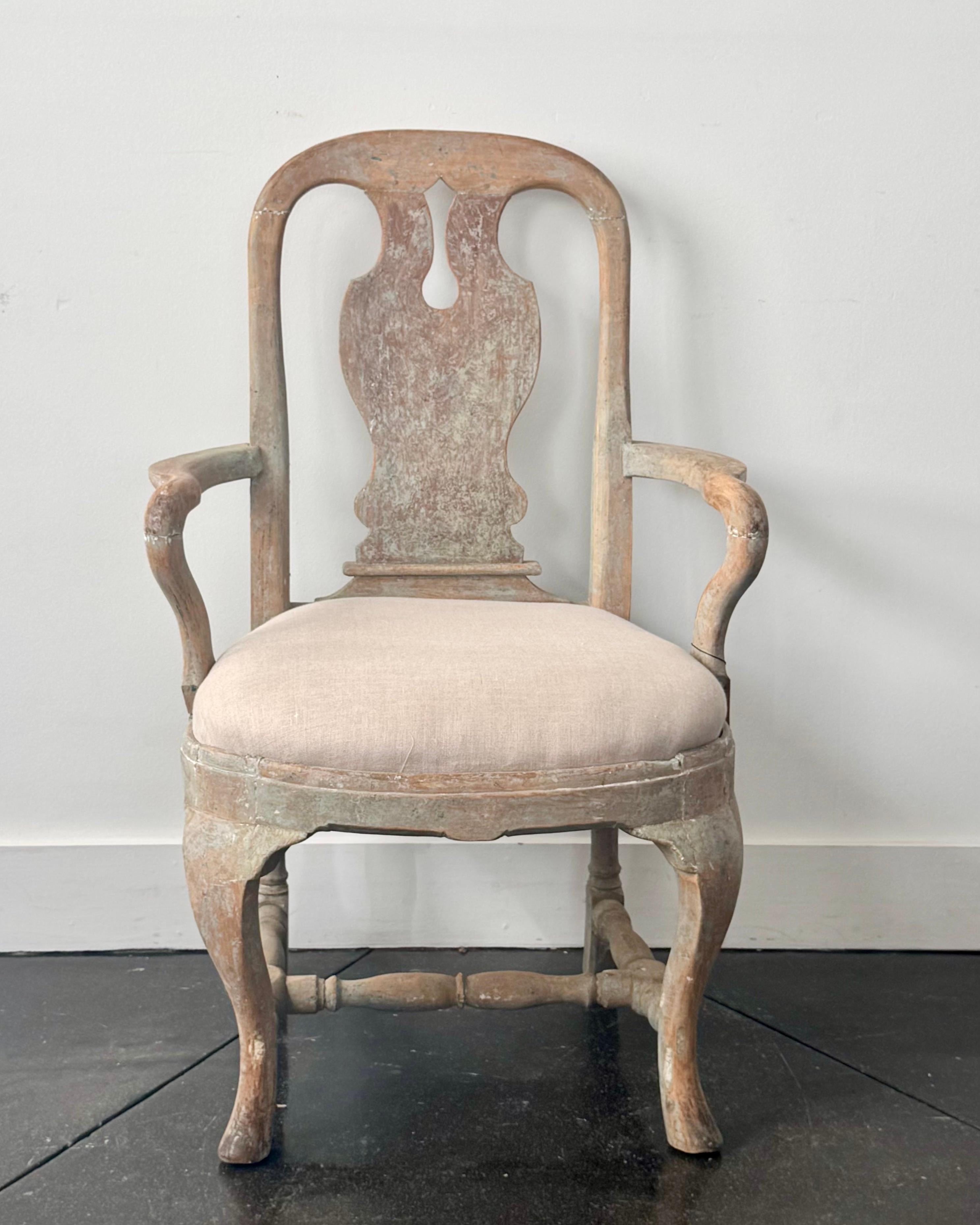 Sillón rococó de época sueca del siglo XVIII, de silueta sencilla, en el que se ha raspado al máximo su acabado original, dejando ver la madera natural. Presenta patas cabriolé talladas con una camilla en forma de H. El asiento abatible retapizado