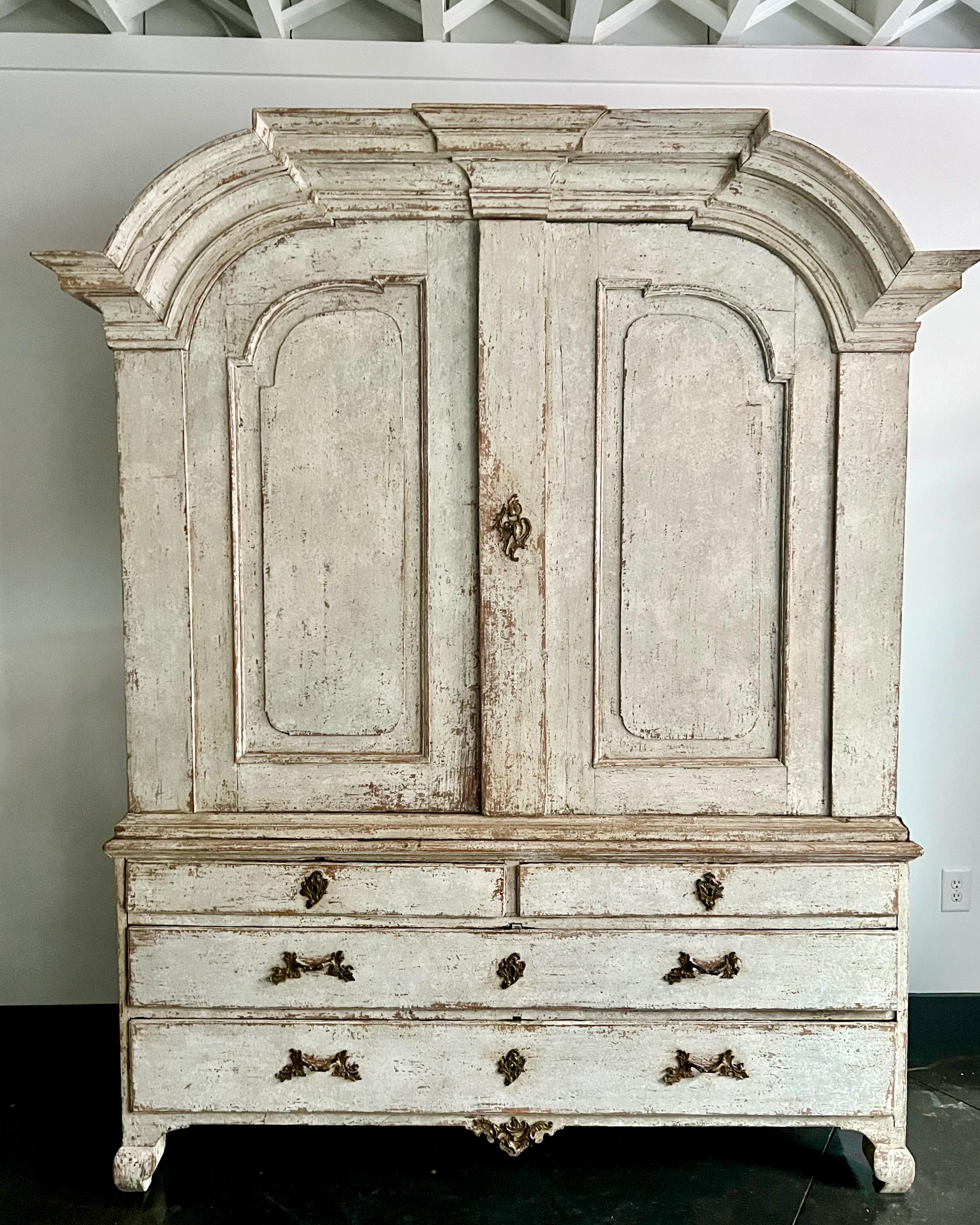 Large 18th century Swedish Rococo Period Cabinet in two pieces with wonderful arched cornice, original hardware, shaped apron and cabriole legs.Upper unit features two shelves, bank of small 3 drawers and a notched spoon shelf in blue patina. All