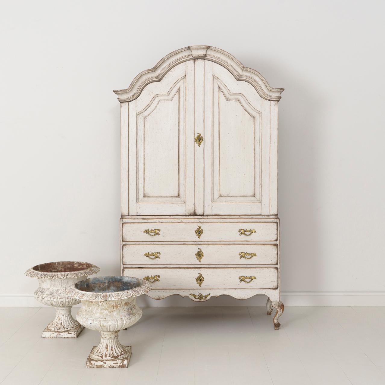 An 18th century two-part Swedish linen press or armoire from the Rococo period with original gilded bronze hardware, locks, and keys. This cabinet is beautifully proportioned with a gracefully arched pediment cornice and curvaceous cabriole legs.