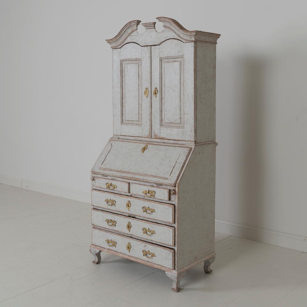 A Swedish Rococo period slant-front secretary from the 18th century in two parts with original bronze hardware. The slant-front opens to reveal 9 small drawers and a centre pigeon hole with shelf all behind the writing surface. The desk surface