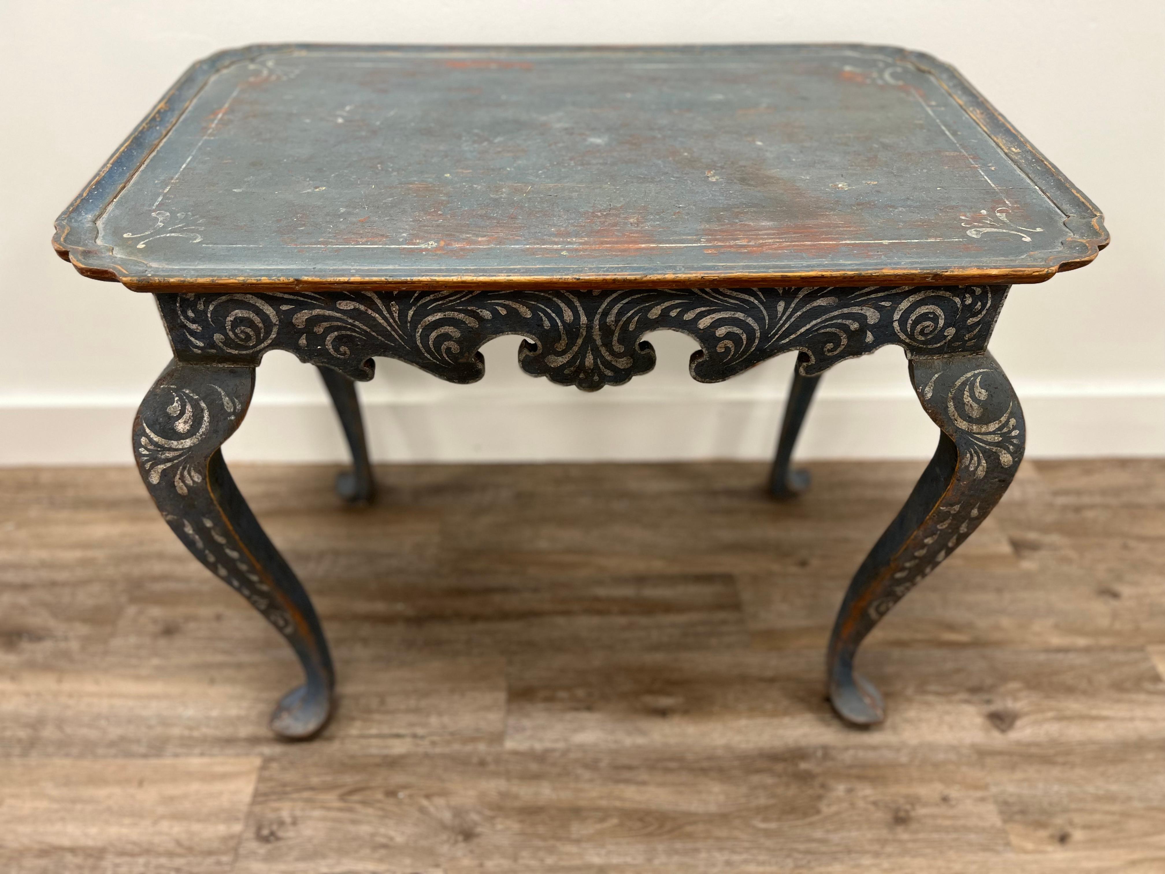 A Swedish Rococo table with rectangular top and scalloped corners, over decorative carved base atop cabriole legs. In original dark blue paint with hand-painted white scroll design.