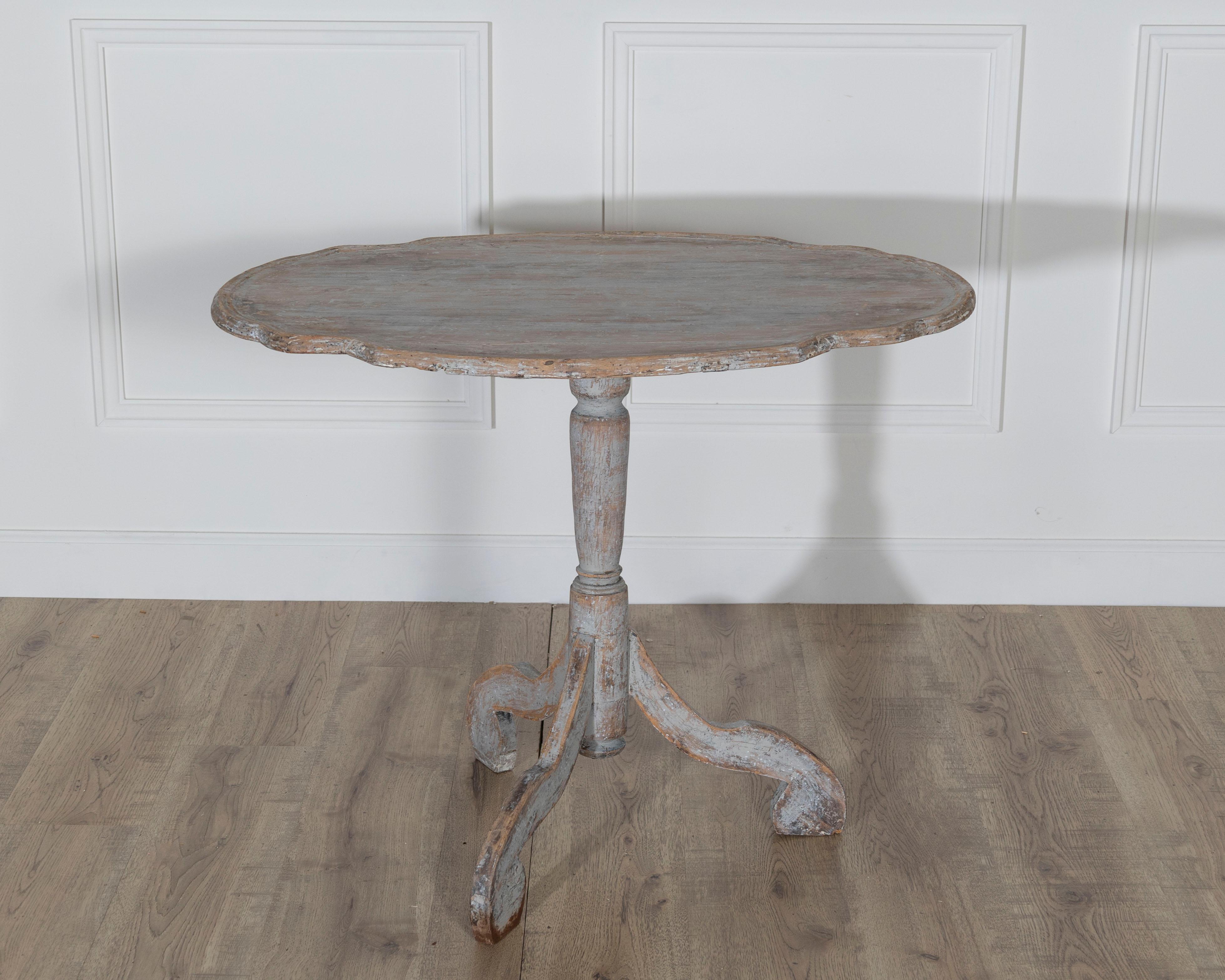Authentique table à plateau basculant de style rococo suédois du XVIIIe siècle, remarquable par sa forme sculpturale et sa construction originale. Le plateau rond et festonné repose sur un piédestal tourné en balustre, soutenu par trois pieds