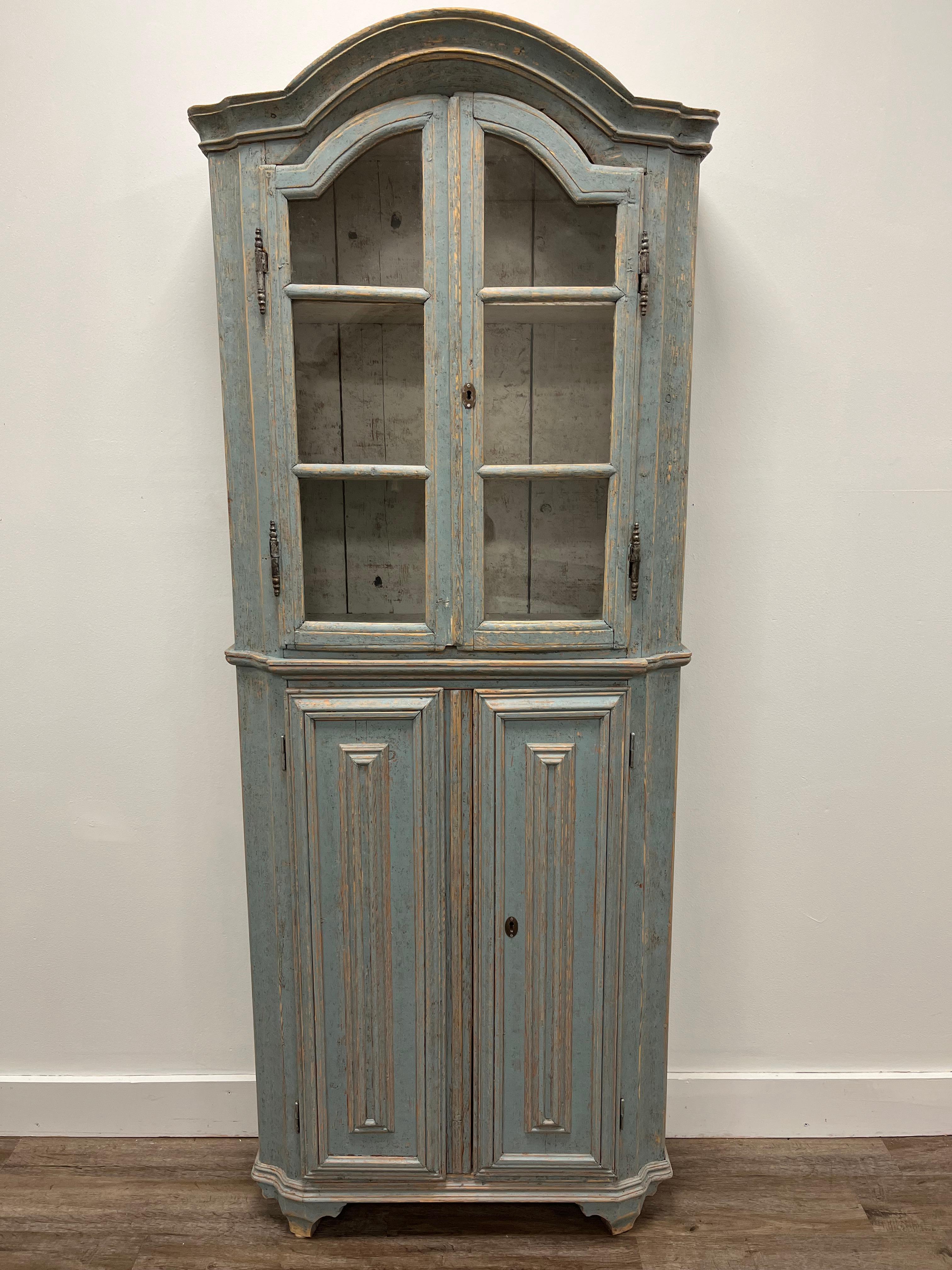 An unusually narrow one-piece Rococo vitrine with original brass hardware and locks. The lower cabinet has later hinges. The upper cabinet has three shelves under a bonnet top with glass doors. The lower cabinet has three shelves behind vertical