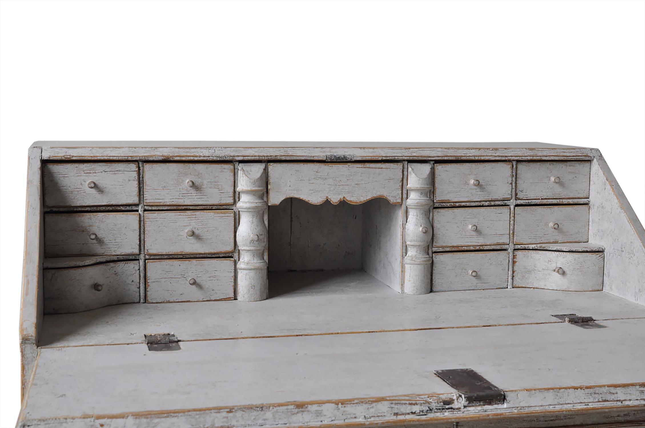 This 18th century Swedish desk features a slant front which opens to eight storage drawers, beneath this are two further short drawers and two long drawers - useful for storage. The drawers each have a decorative edge. This piece is light grey in