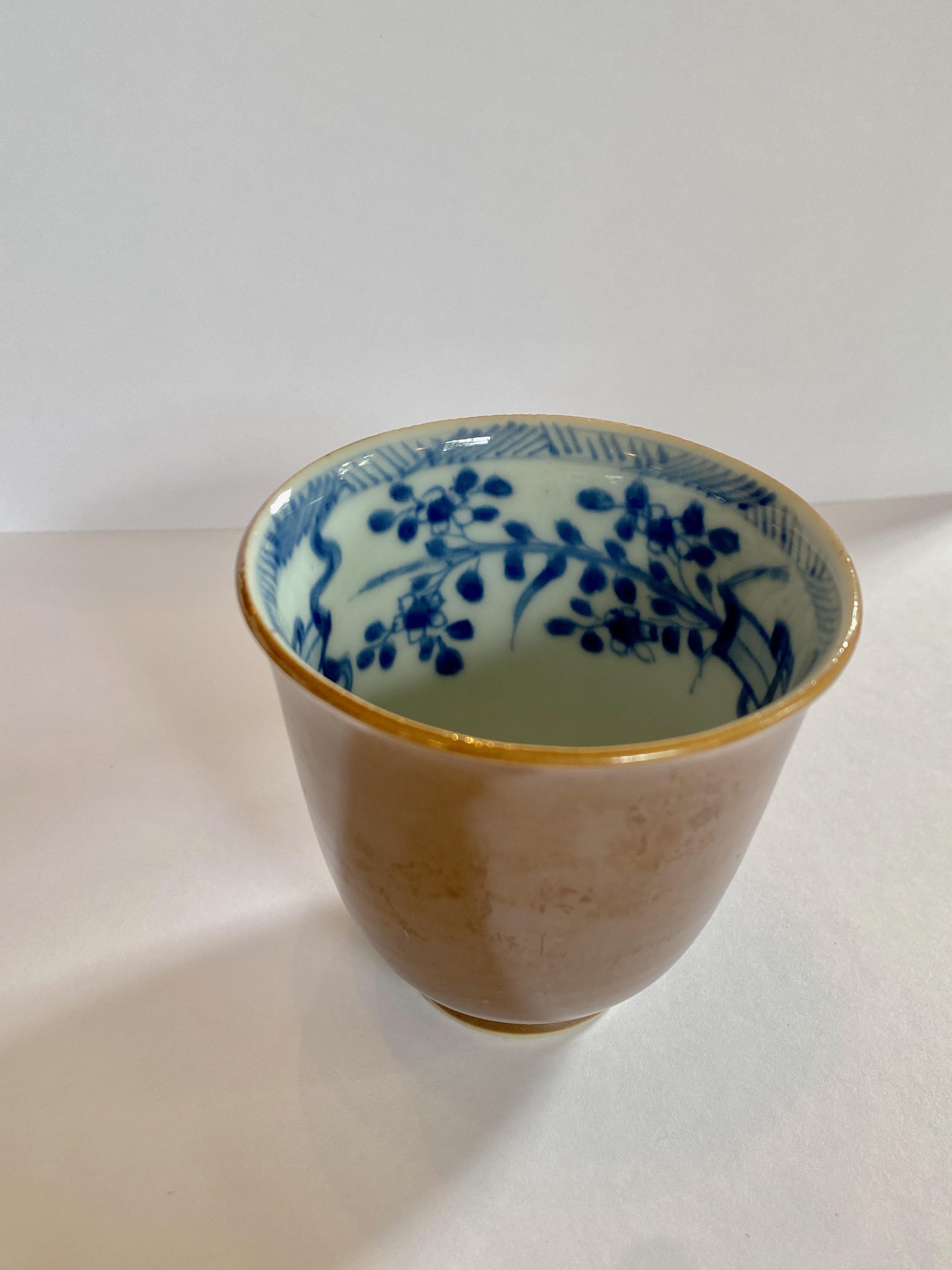 18th century porcelain cup, Qianlong period (1735-1796) of the Qing Dynasty. 
This elegant cup has a nearly iridescent cafe au lait (light brown) exterior glaze and blue and white interior decorated with ribbons and flowers, making a delightful