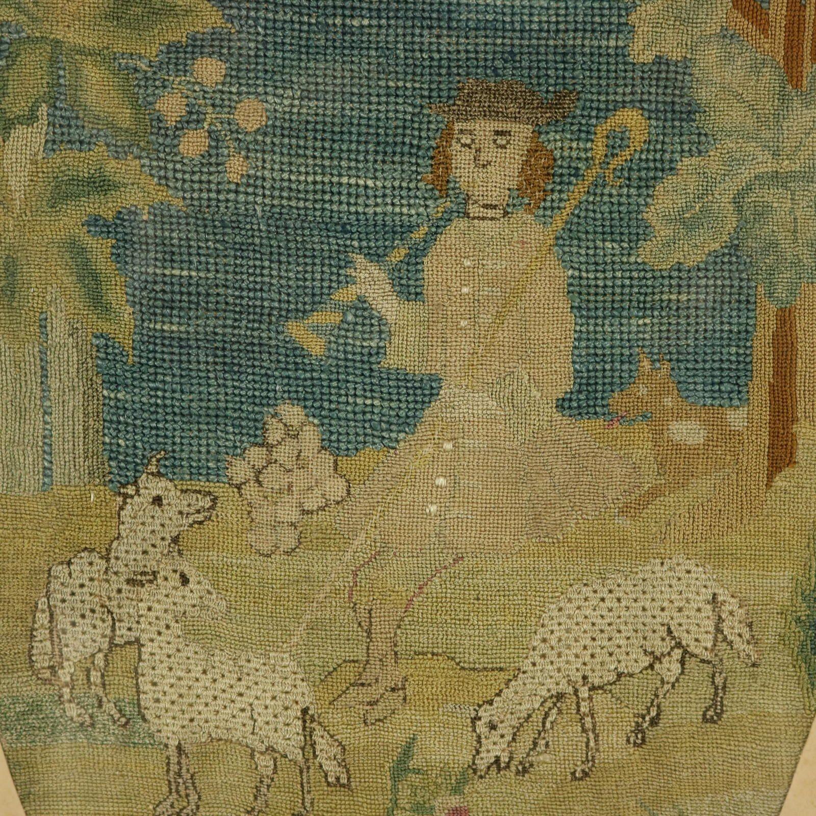 An 18th Century tent stitch silkwork embroidery of a shepherd with his flock of sheep. The piece is worked in tent stitch, using silk threads. Colours blue, green, silver, brown and pink. Subject depicts a shepherd holding his crook and a pipe, with