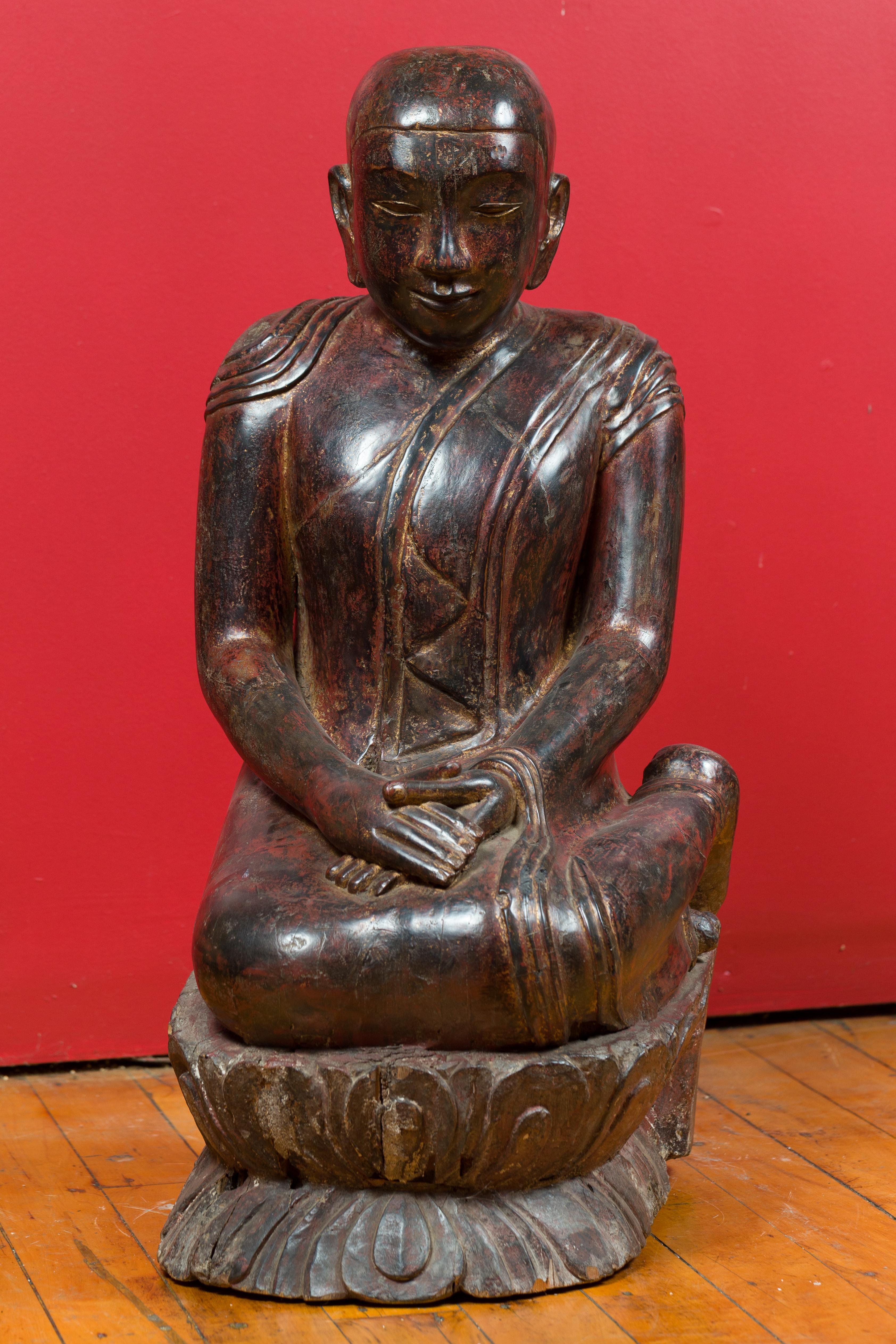 A Thai hand carved lacquered wood sculpture from the 18th century depicting a seated monk. Created in Thailand during the 18th century, this carved statue features a serene seated monk with his hands resting on his knees, his feet to the side. The