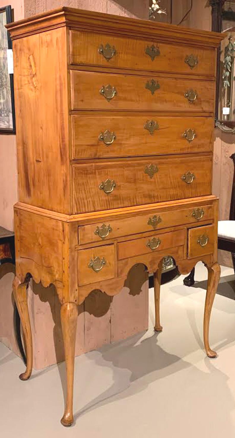 A nice two part curly maple highboy, its upper case with molded cornice surmounting four graduated drawers, over a lower case with one long drawer over three fitted drawers, all with replaced brasses, over a beautifully carved skirt, all supported