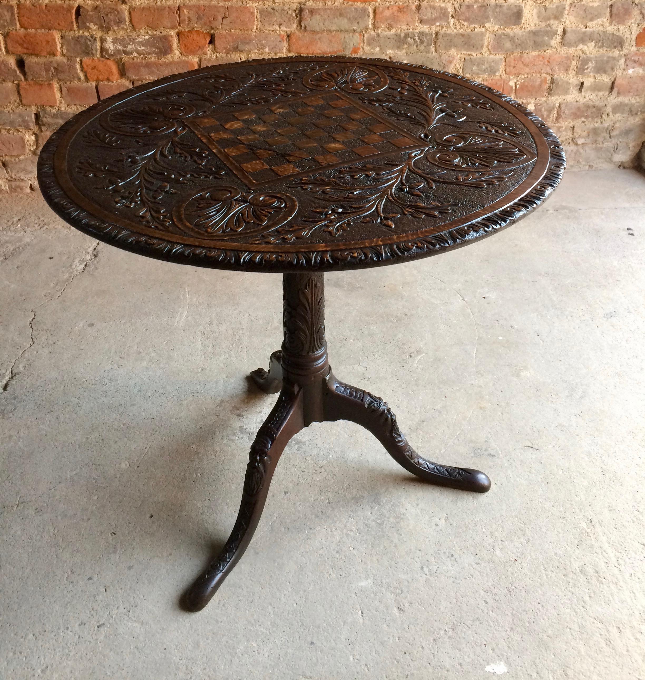 Antique 18th century solid English oak tilt-top tri pod table dating to circa 1780, the heavily carved circular top featuring carved vines with acorns, hearts and chess board, the carved supporting base with forged iron hinges. And three heavily