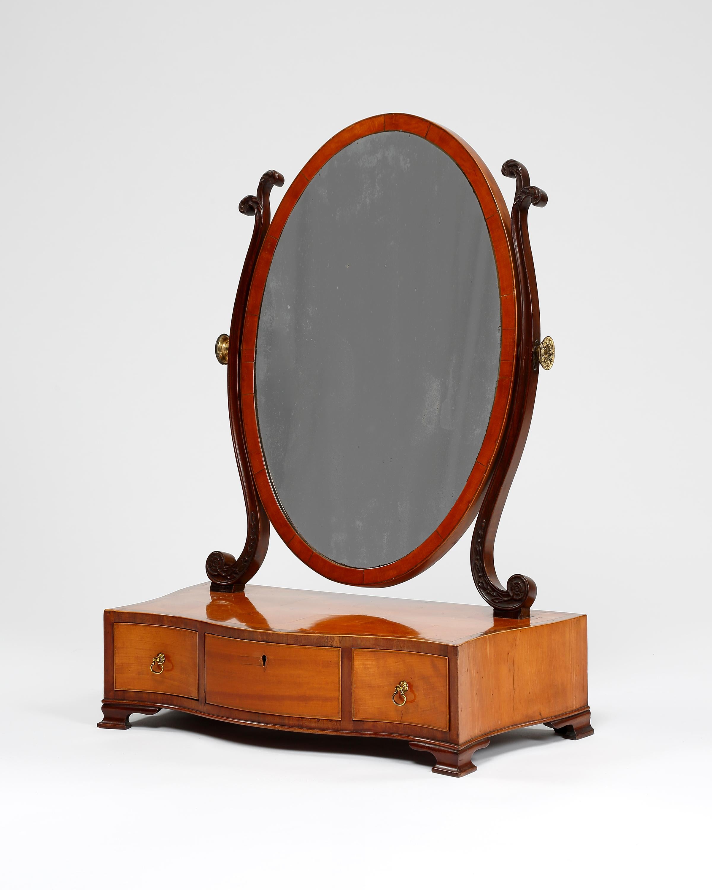 A George III period satinwood veneered toilet mirror. Serpentine sides and front, having three small drawers, edged in boxwood throughout. Possibly the original oval mirror plate with fine s-shaped carved supports, English, circa 1775.
