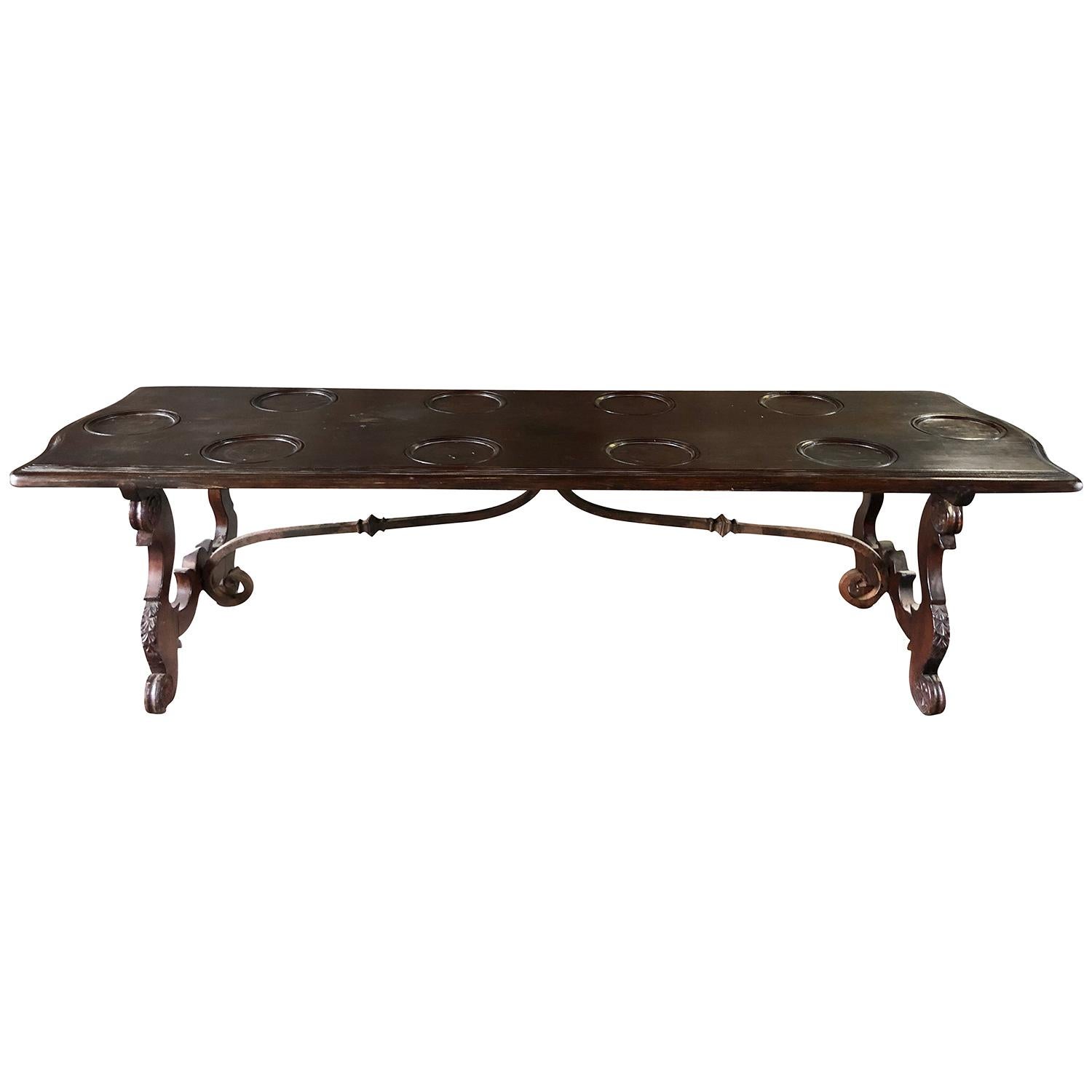 A rectangular, antique very long Tuscan Renaissance dining room table made of hand crafted Walnut, in good condition. The top of the Italian center table has a dark original patina with carved round plate inserts supported by two very ornate wrought