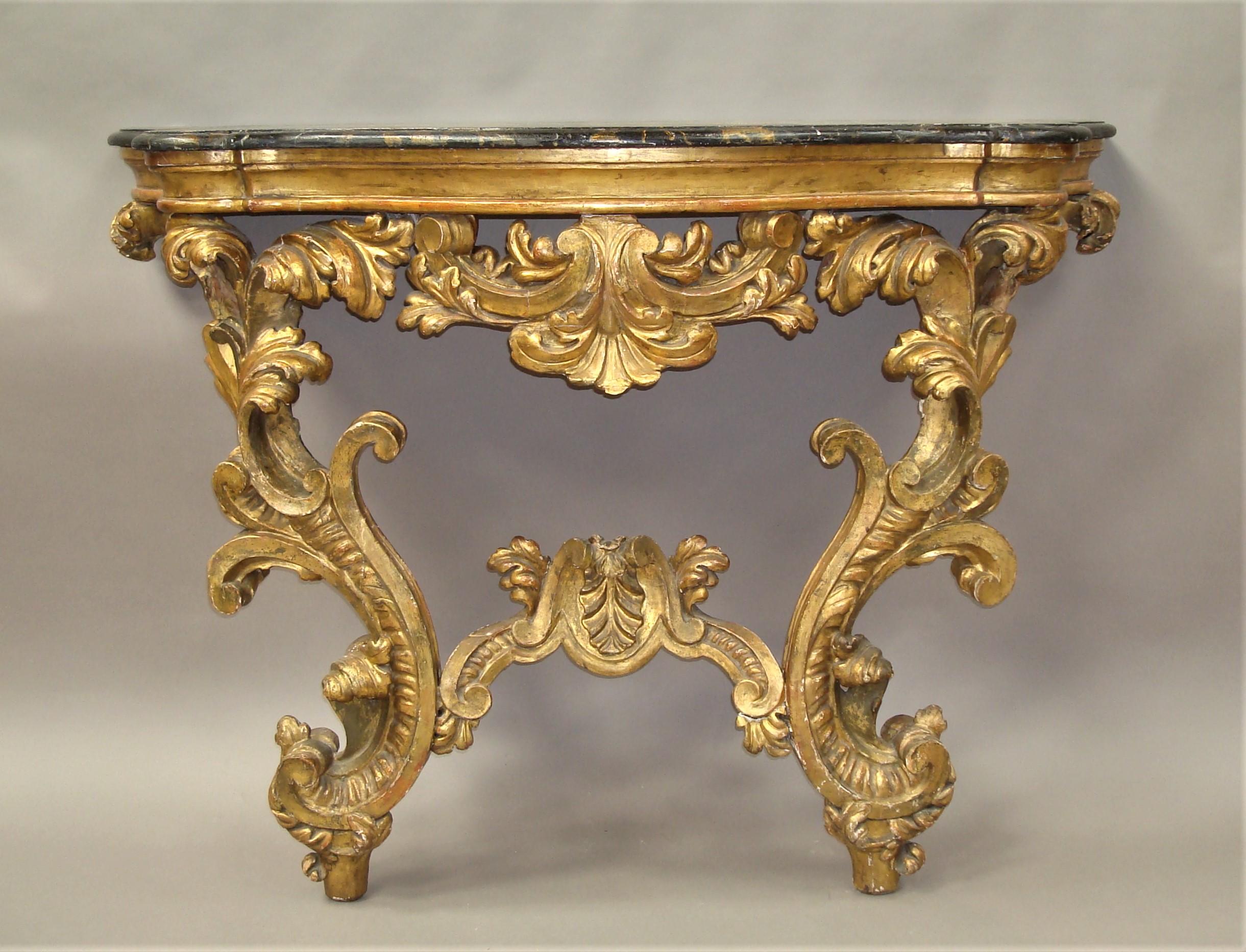An impressive 18th century Venetian Rococo giltwood console table of serpentine form; the 19th century strikingly painted wooden top, simulating portio marble; with a moulded edge and protruding round corners, above the shallow giltwood shaped