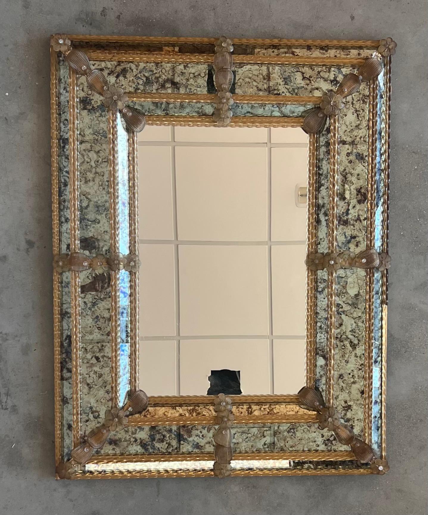 Le miroir vénitien carré présente des panneaux biseautés et des reliefs sculptés.  Le miroir a été fabriqué et argenté à la main. Le panneau central présente une légère finition antiquaire tandis que le pourtour présente une antiquité plus