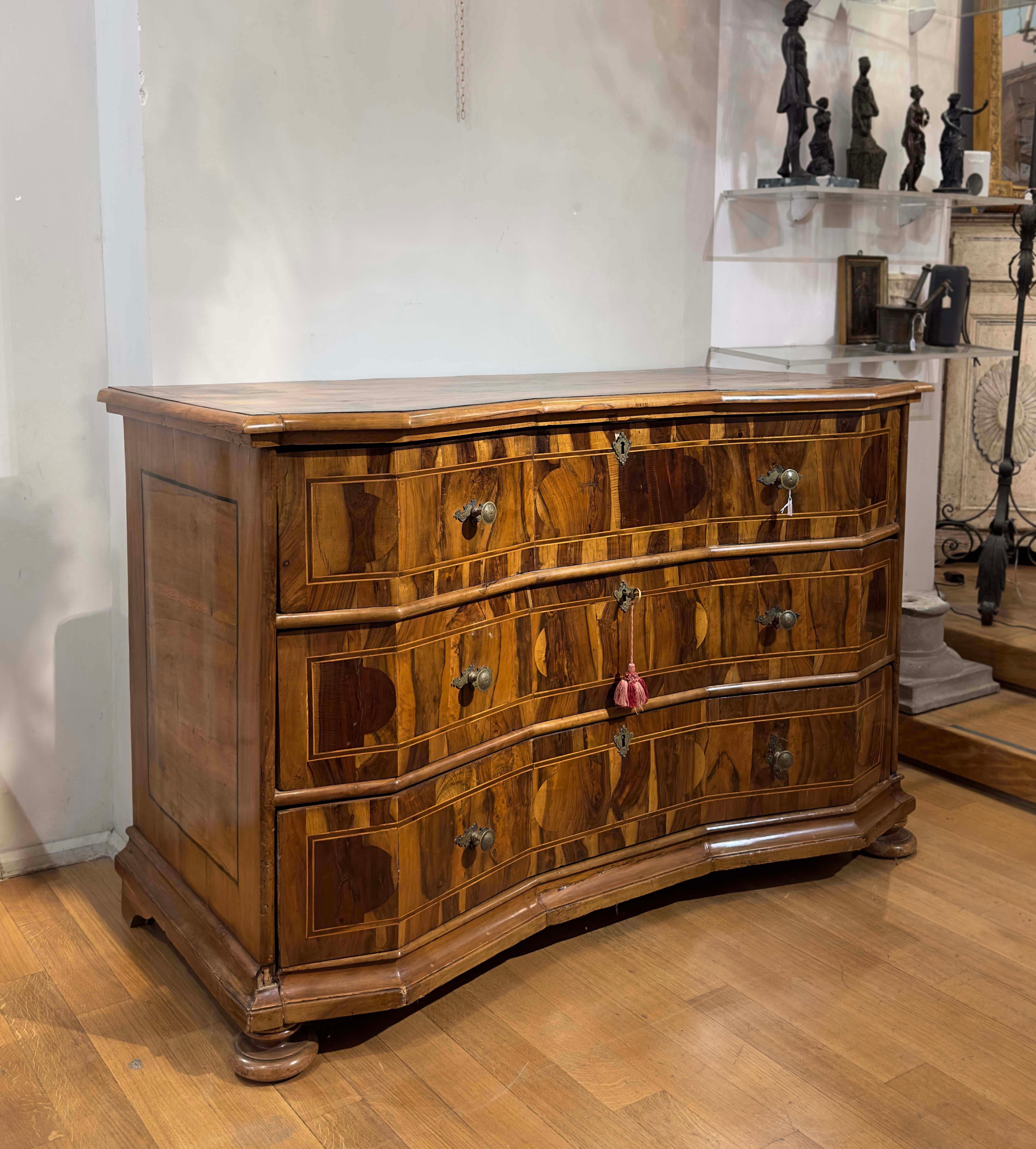 Beautiful veneered chest of drawers in walnut wood and walnut root, enriched with fruit wood fillets. Its uniqueness and sophistication are evident in the wavy front and in the geometric inlay decorations on both the front and the top. The top is